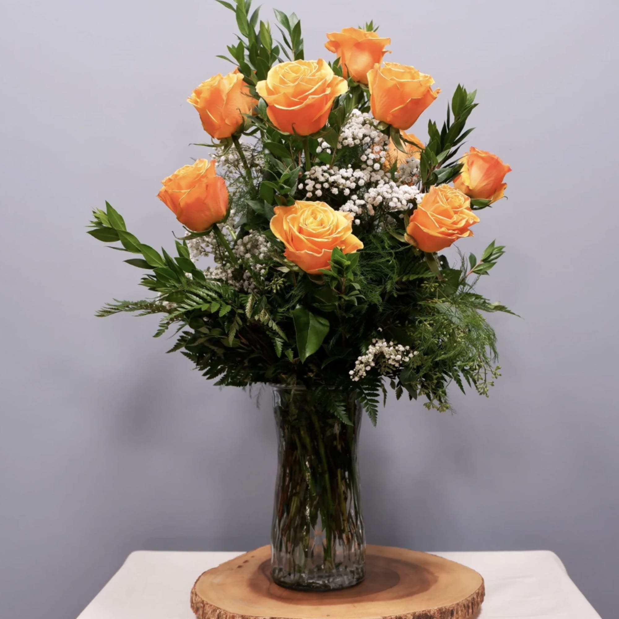 Orange roses arranged in a clear glass vase with baby's breath