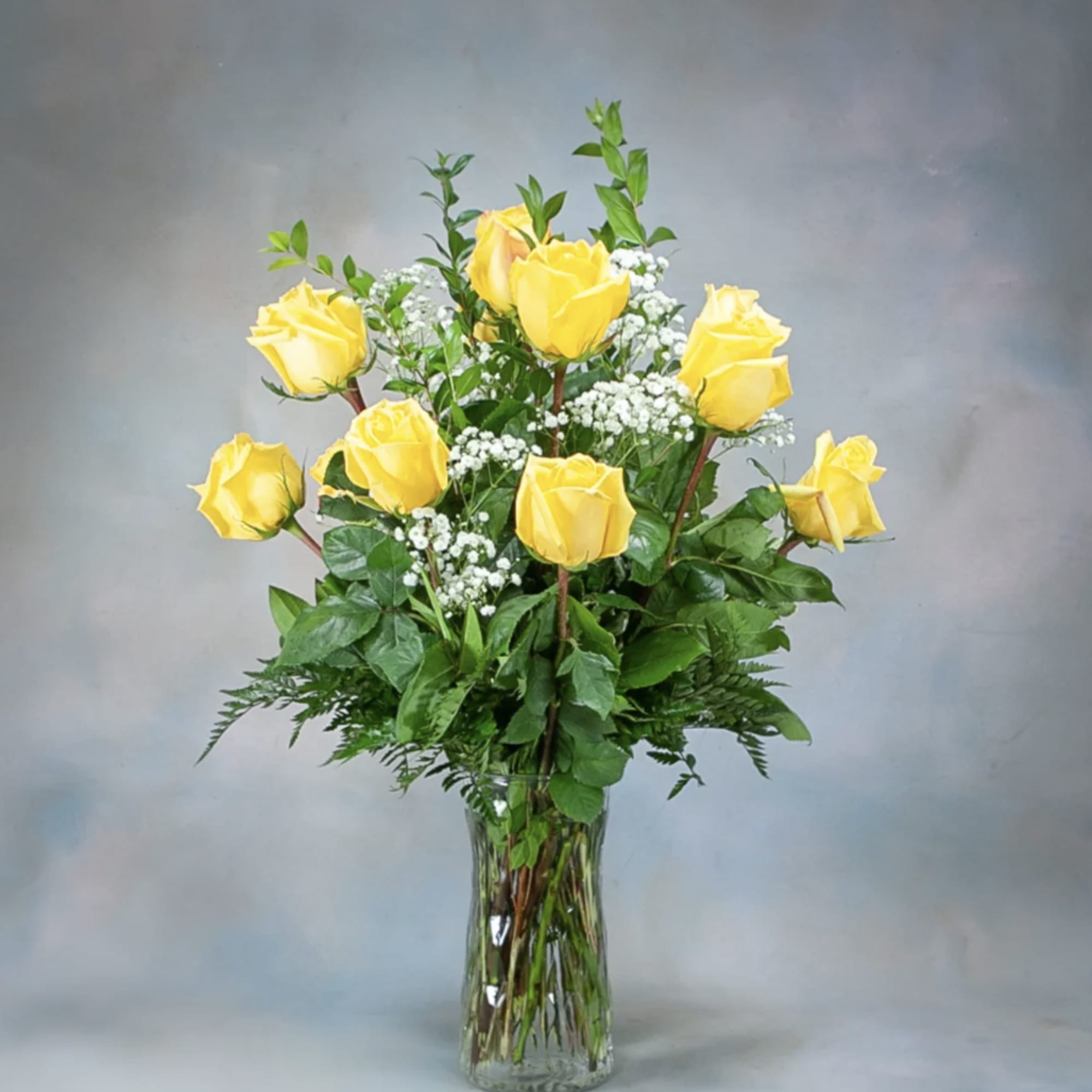 Yellow roses arranged in a clear glass vase with white filler flowers.