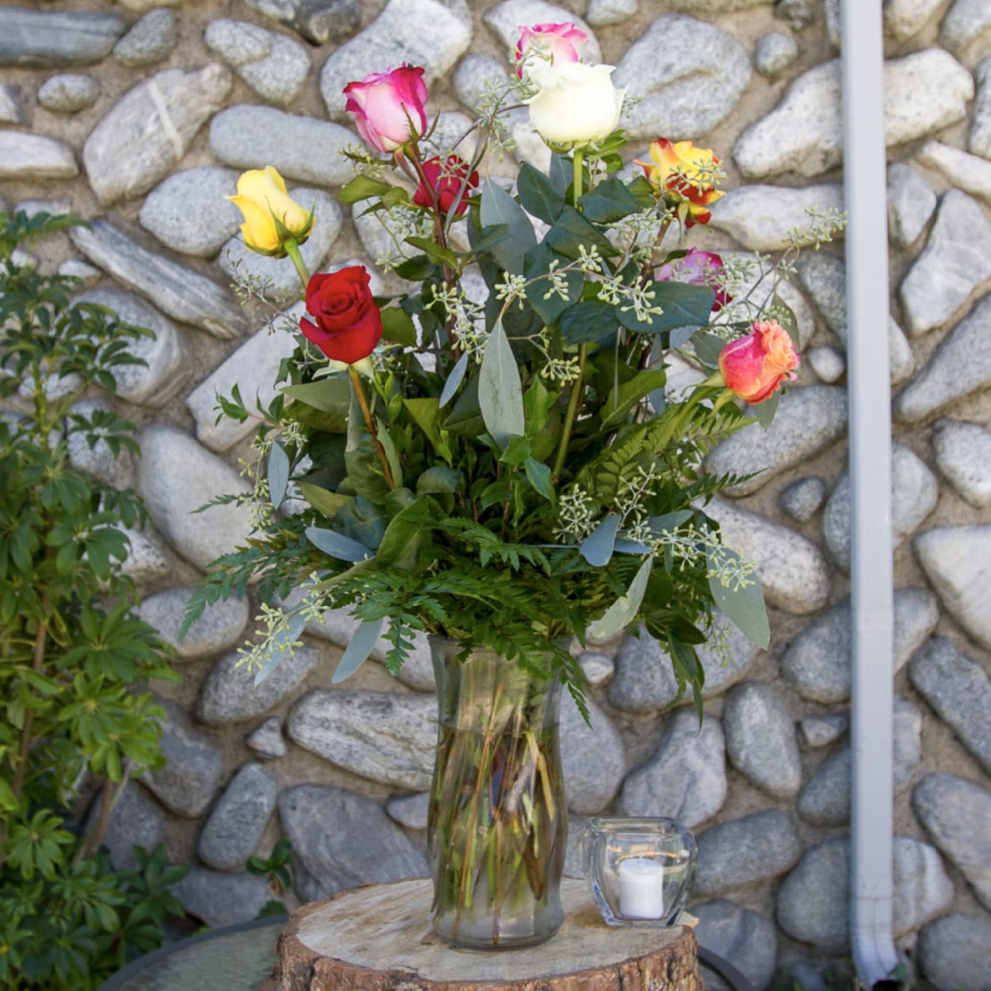 Mixed roses in a clear glass vase with a small candle beside it