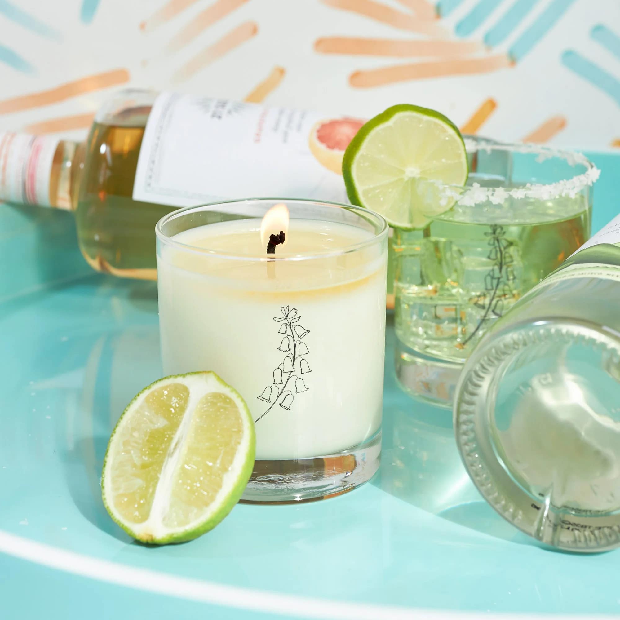 Lit candle with lime slices and several cocktail glasses on a turquoise surface