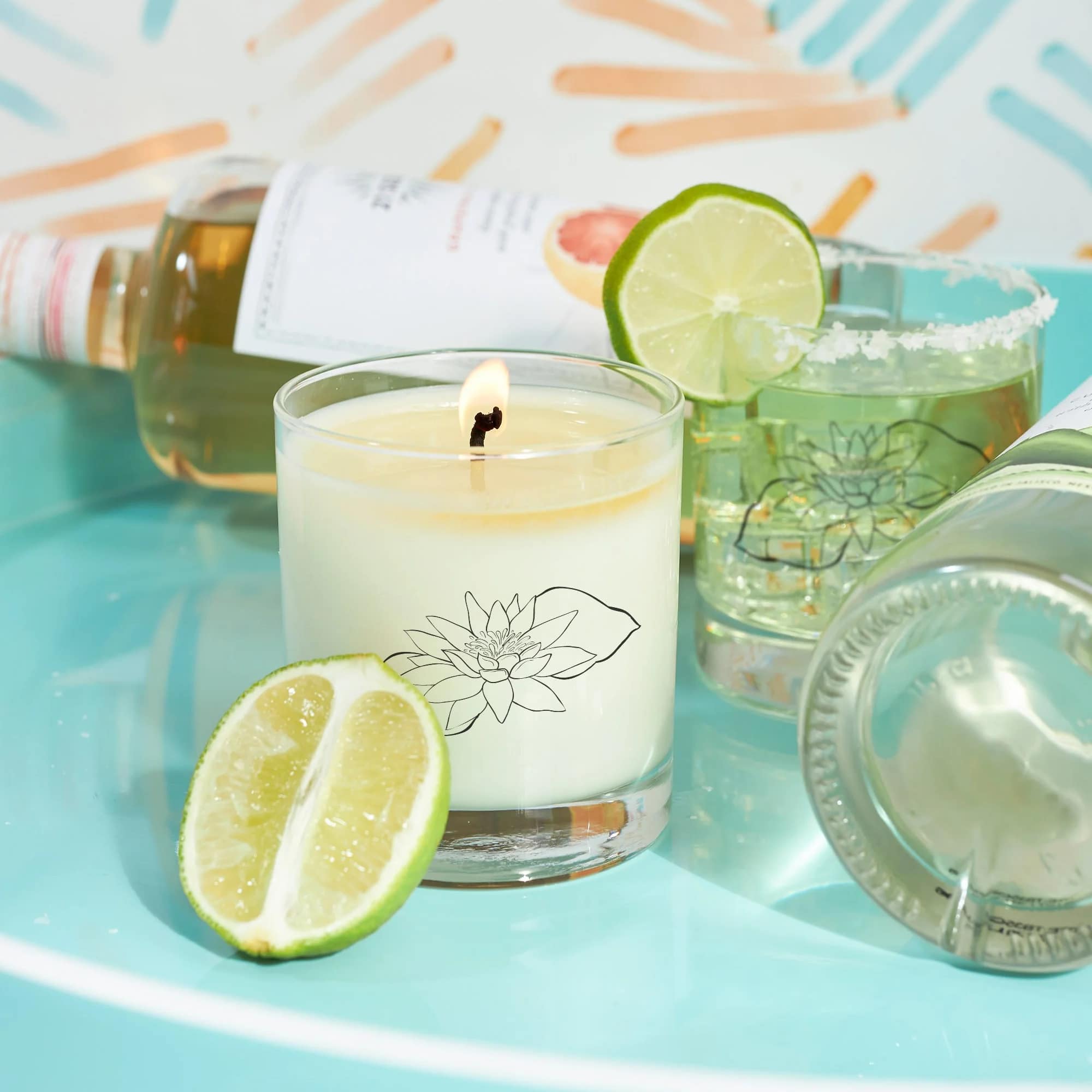 Lit candle with lime slices and several glass bottles on a turquoise surface