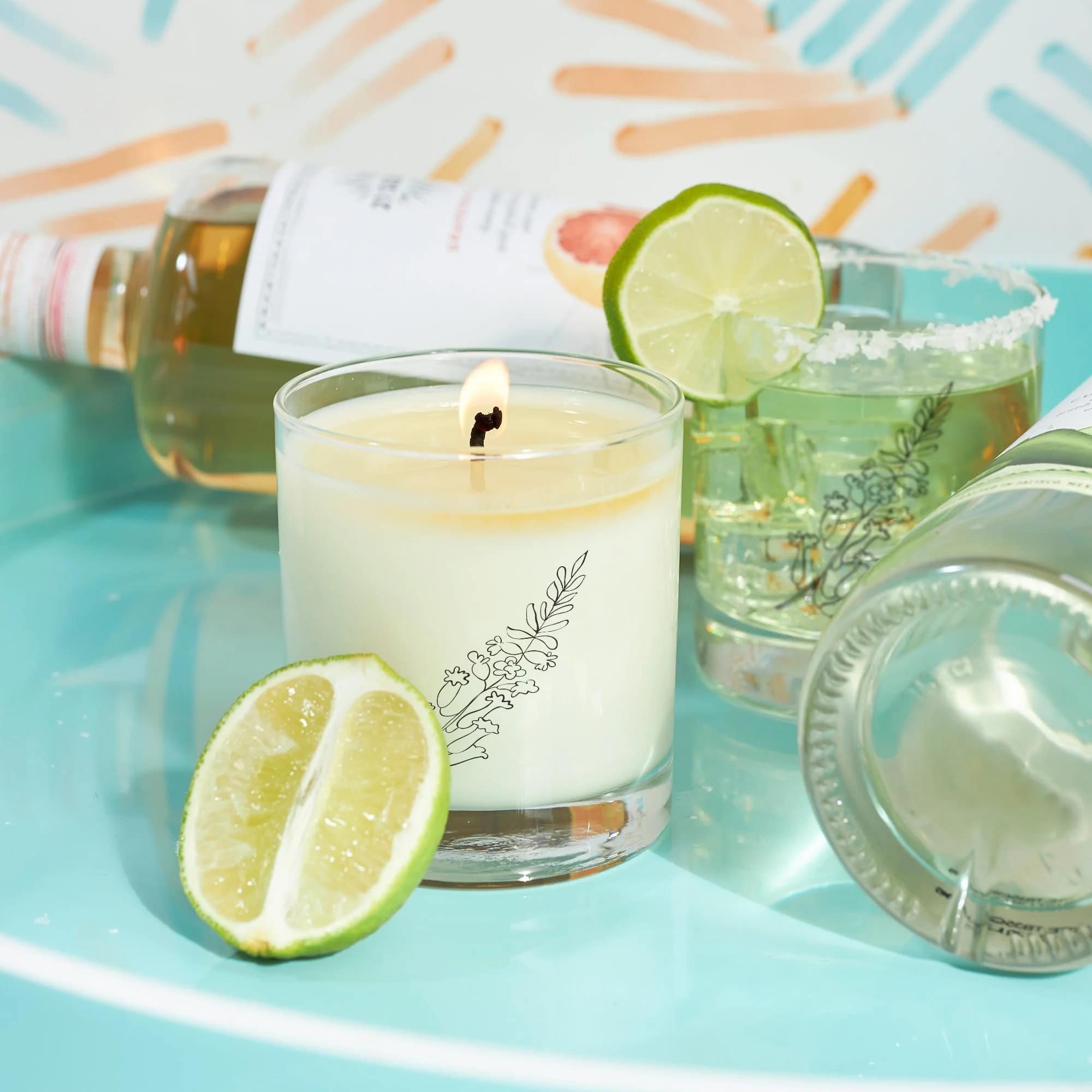 Lit candle in a glass tumbler with lime slices and bottles behind it