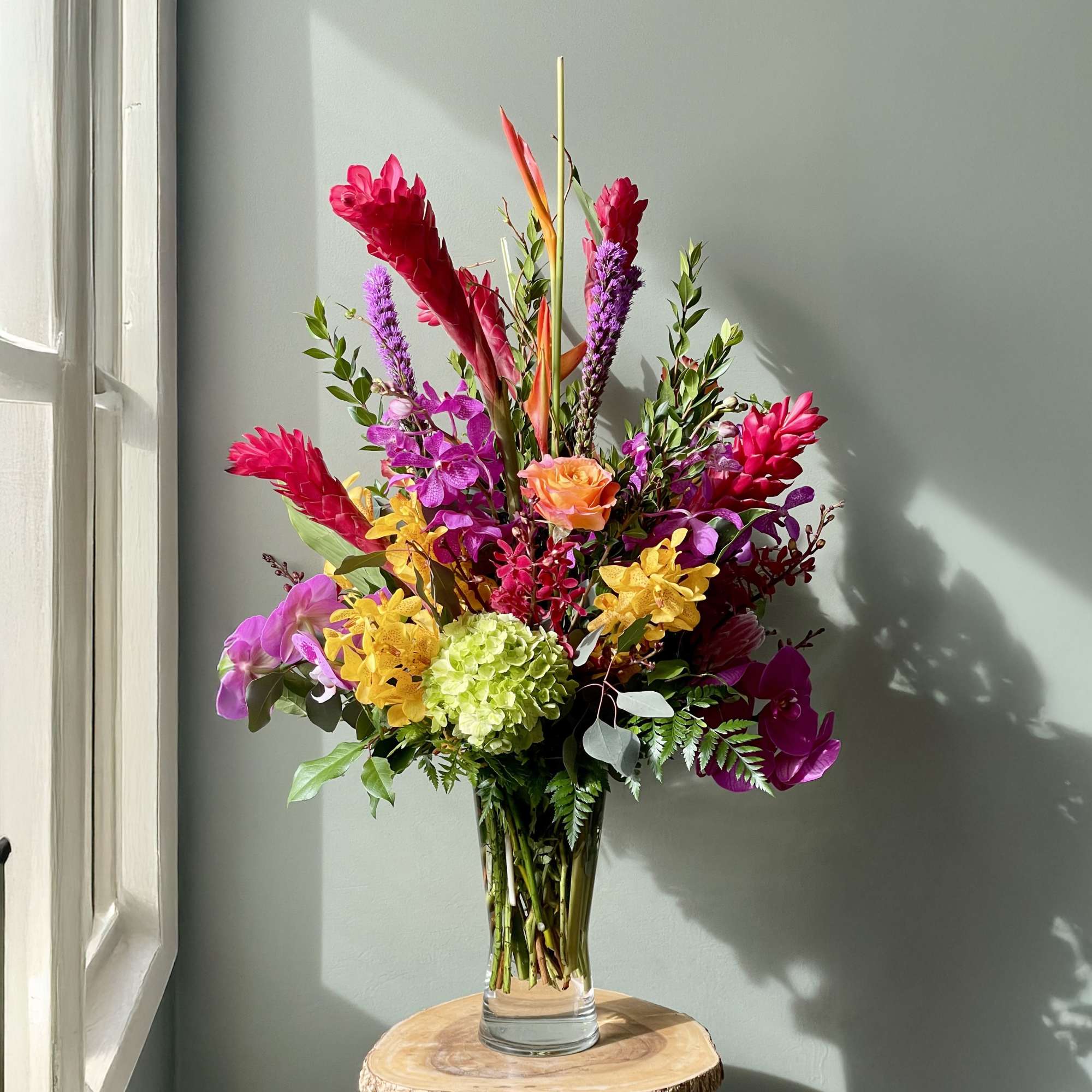 Tall tropical bouquet in a clear glass vase with bright pink, yellow, and orange flowers