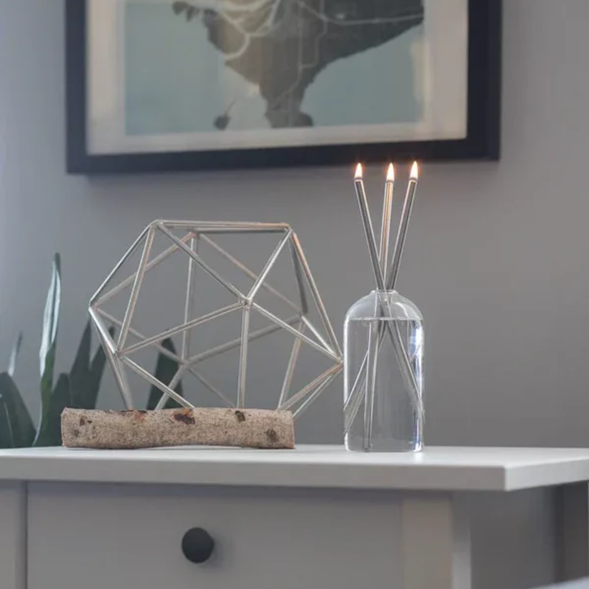 A clear glass diffuser bottle with reed sticks and three lit taper candles on a table