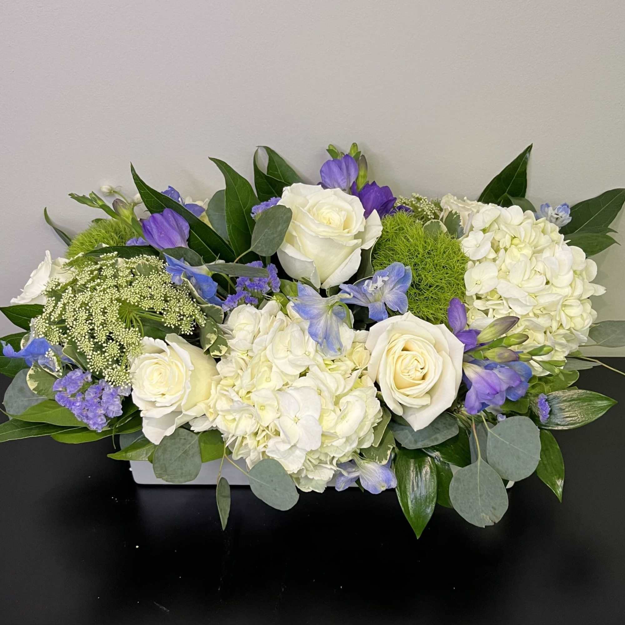 A long and low white vase of beautiful white and green flowers