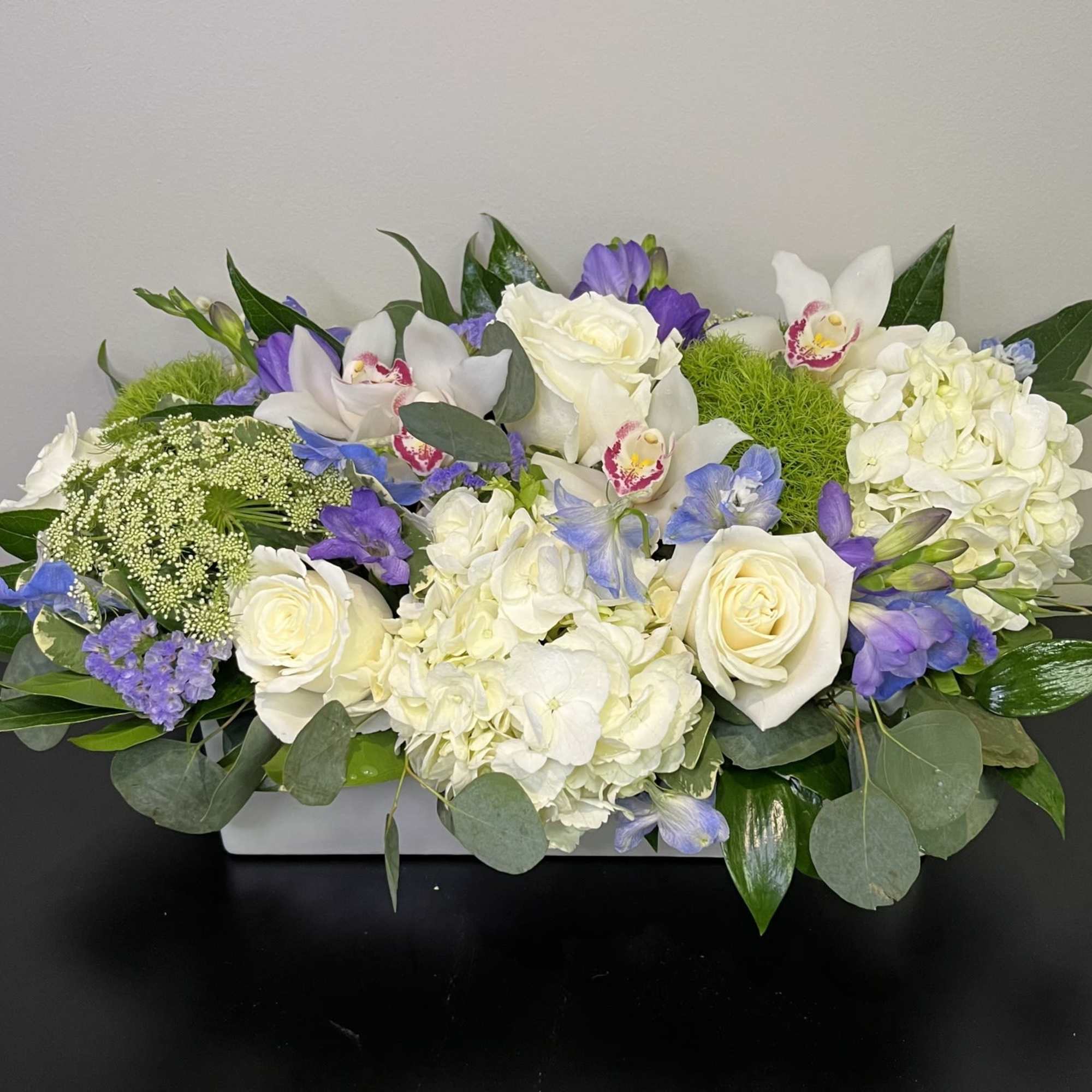 A long and low white vase of beautiful white and green flowers