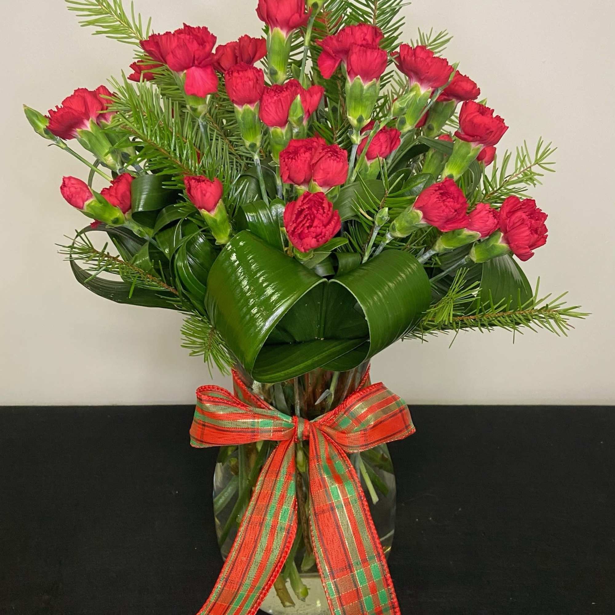 Rich and luscious red mini carnations surrounded by winter greenery, wrapped in