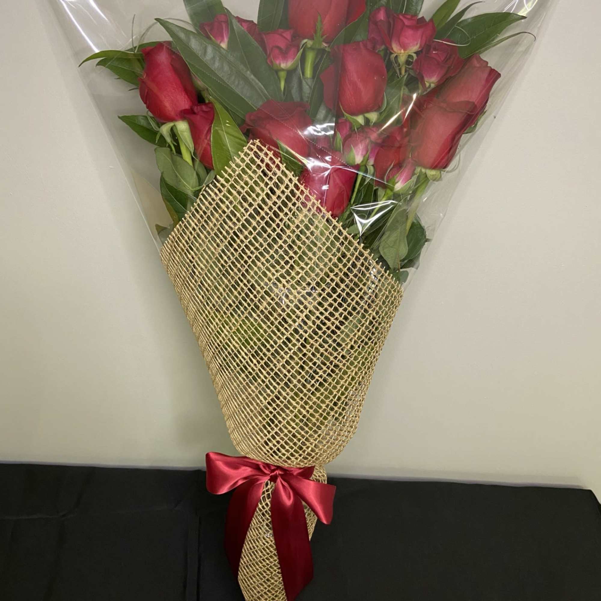 Bouquet of red roses wrapped in clear plastic and burlap with a red ribbon