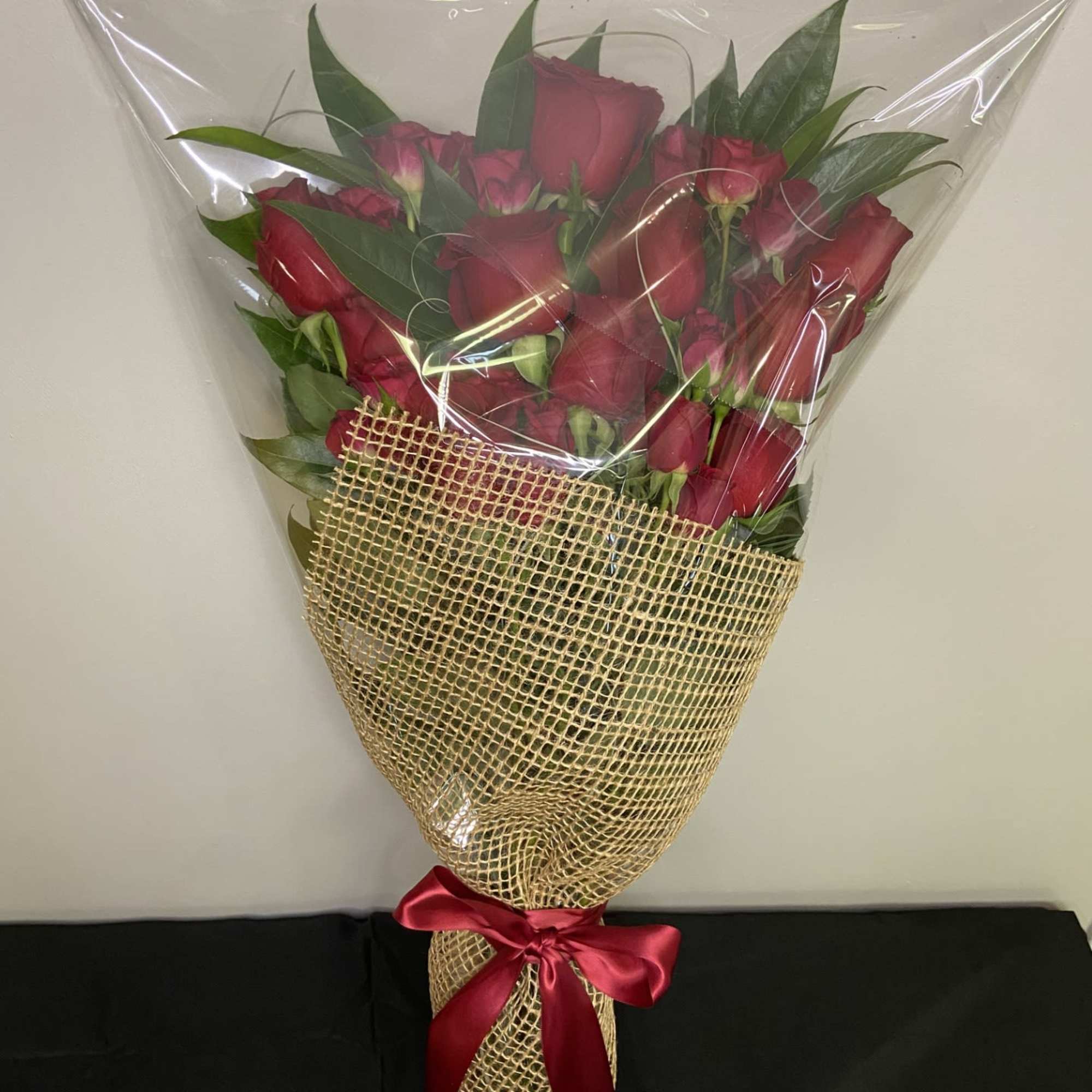 Bouquet of red roses wrapped in clear plastic and burlap with a red ribbon