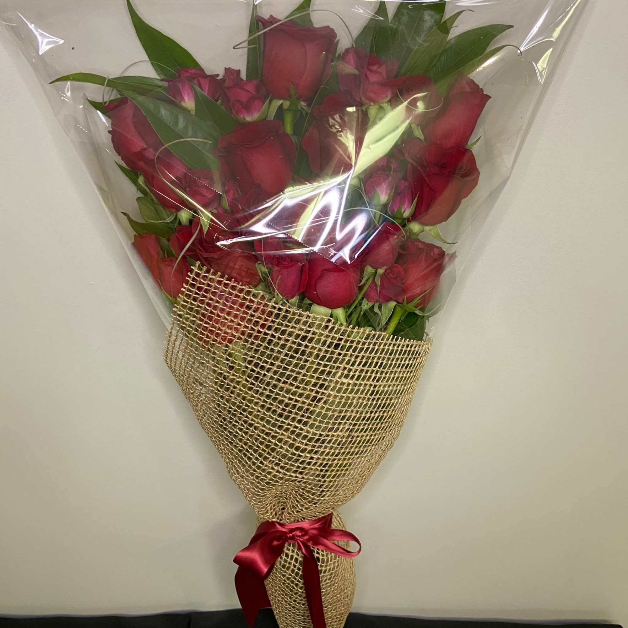 Bouquet of red roses wrapped in clear plastic and burlap with a red ribbon