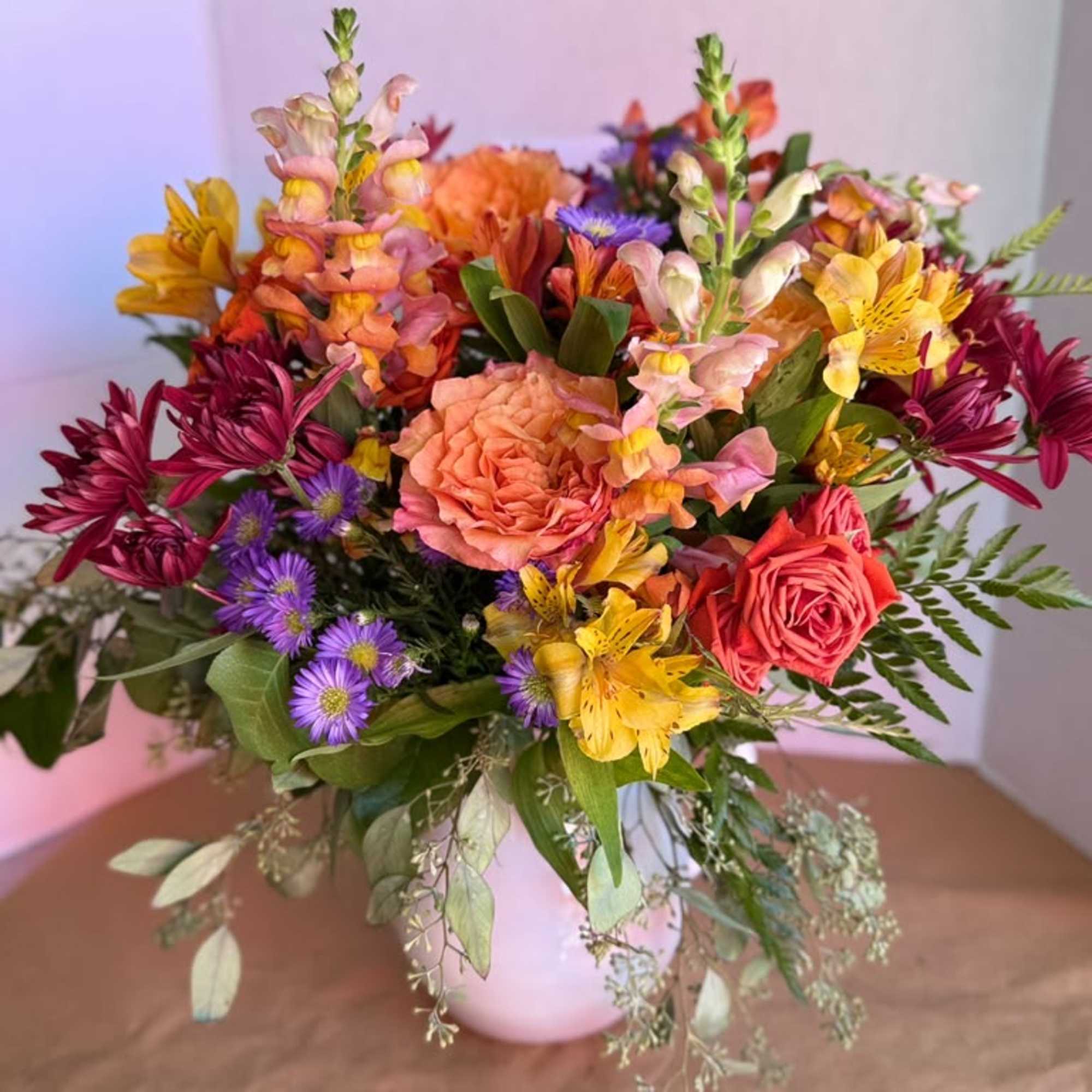 Mixed bouquet of pink, orange, yellow, and purple flowers in a white vase