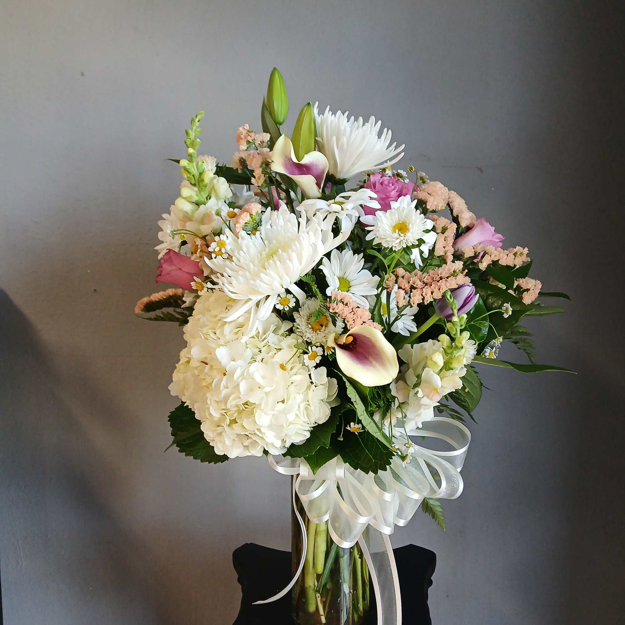 Mixed bouquet of white, pink, and purple flowers in a glass vase with a white ribbon