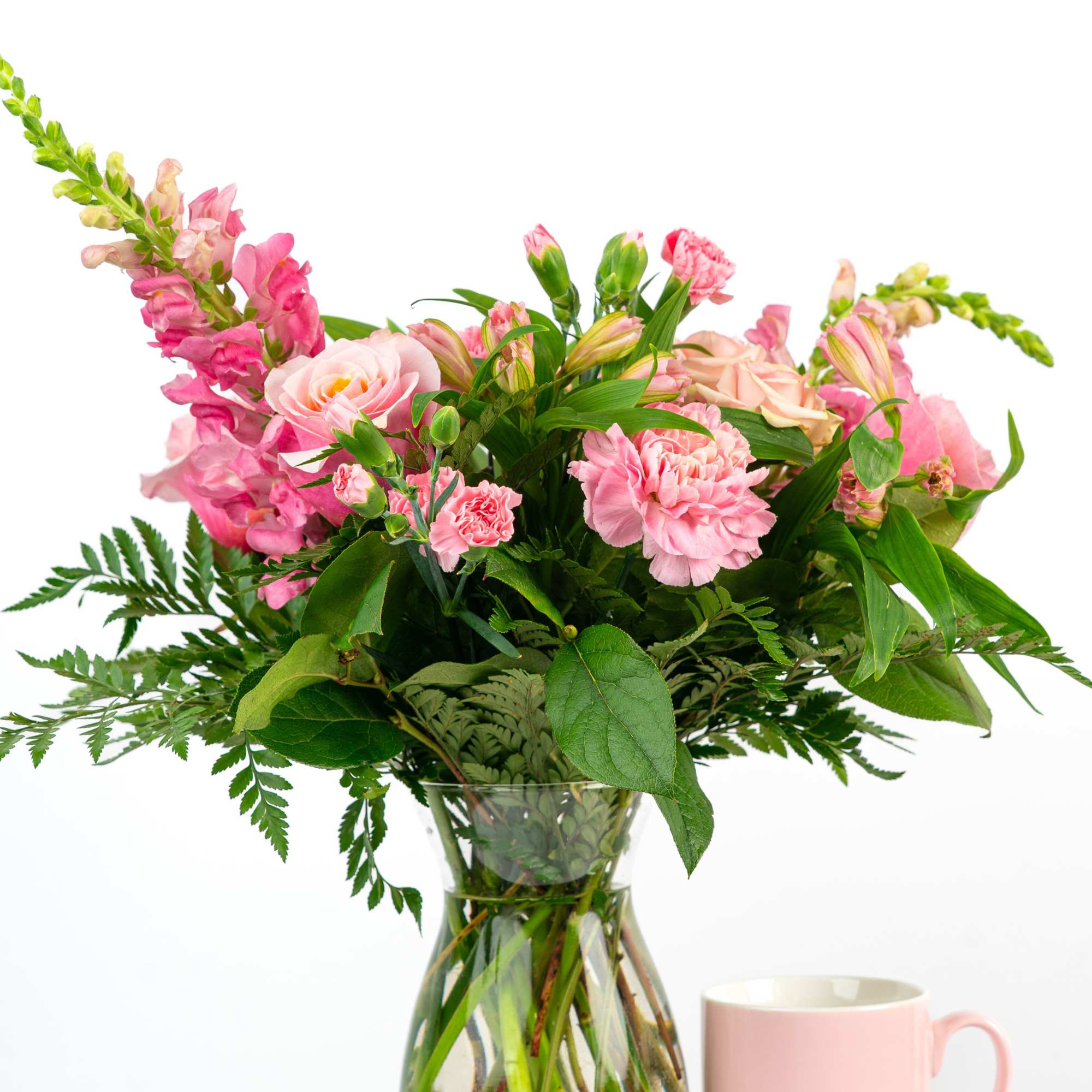 Pink mixed bouquet in a glass vase beside a pink mug