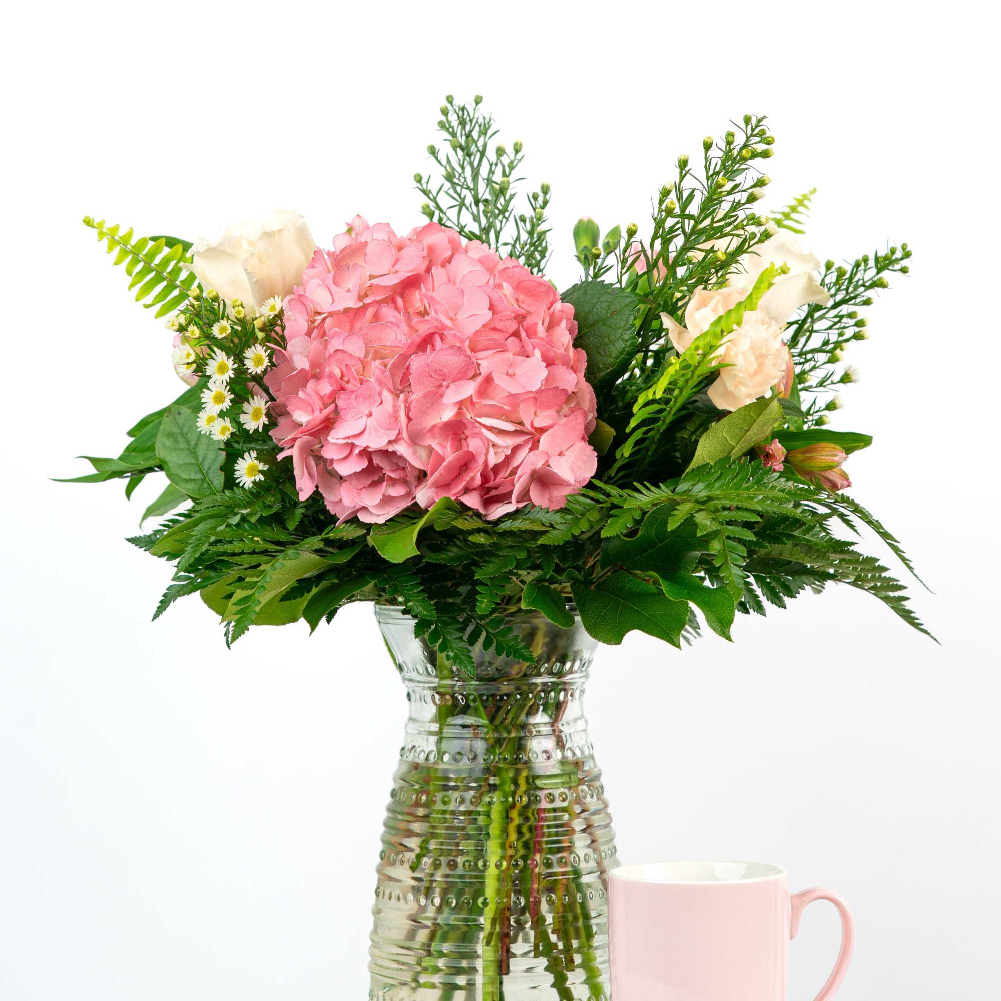 Pink hydrangea bouquet in a glass vase with a pink mug beside it