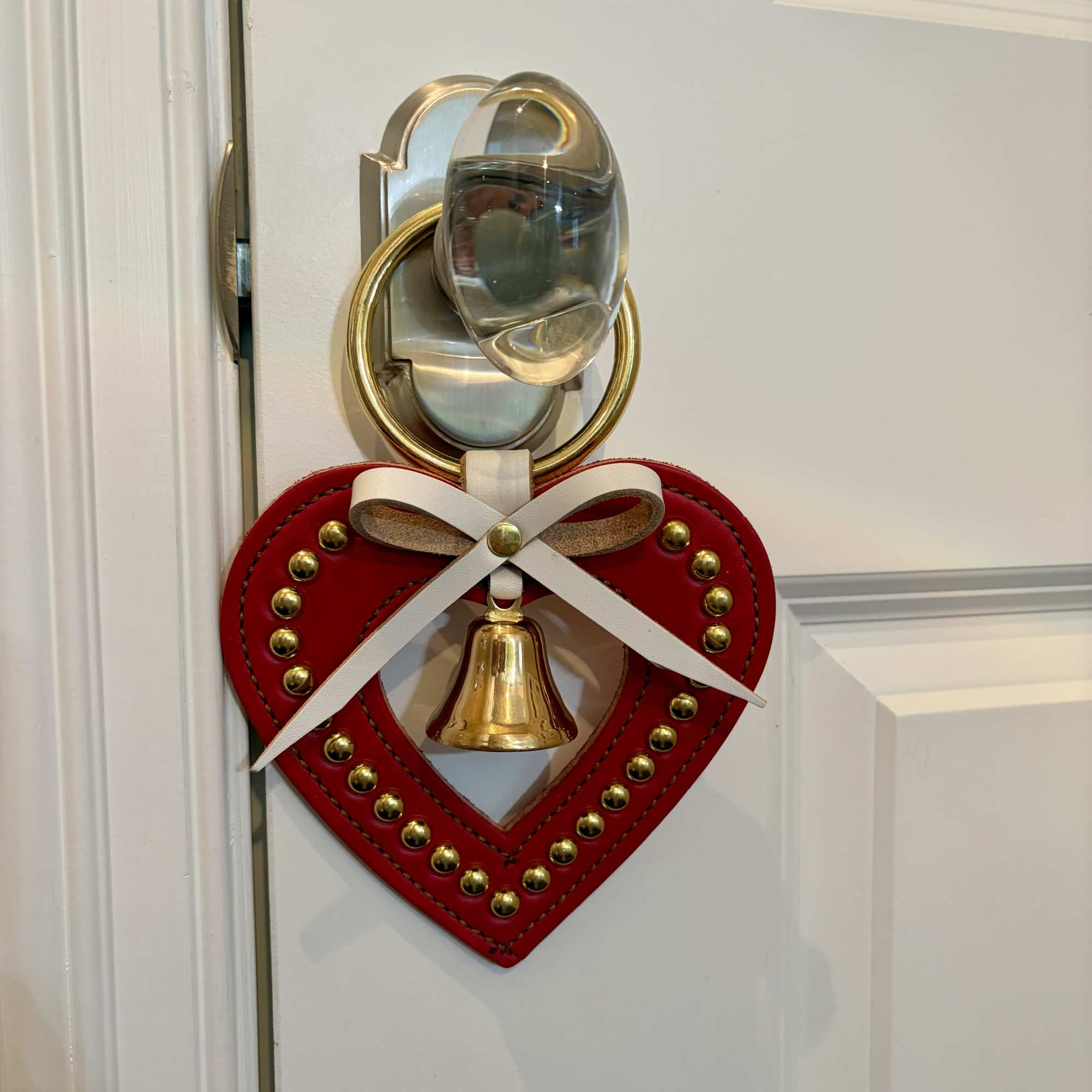 Red heart-shaped door hanger with a gold bell and white bow