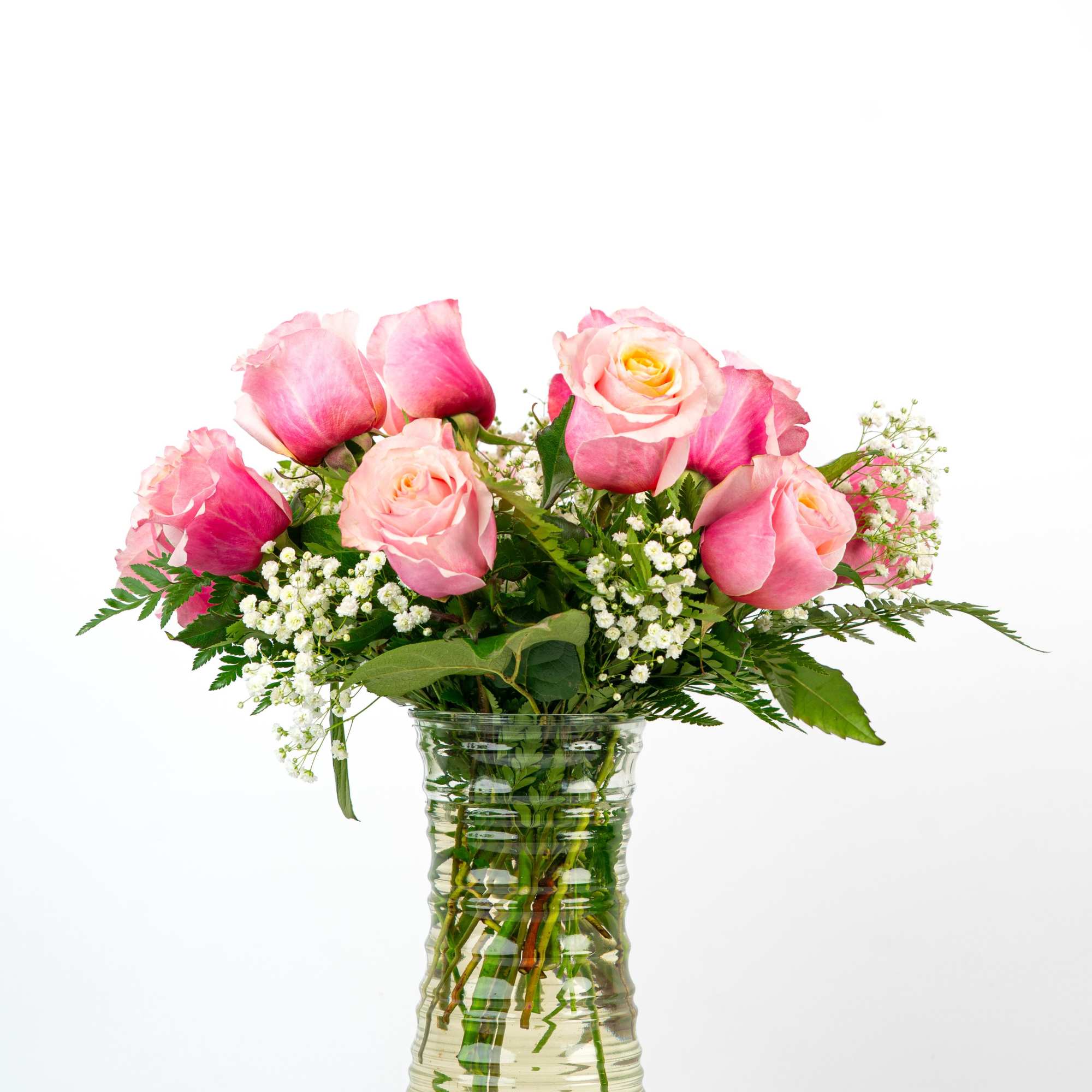 Tall clear glass vase of pink roses with white filler flowers arranged in a loose bouquet