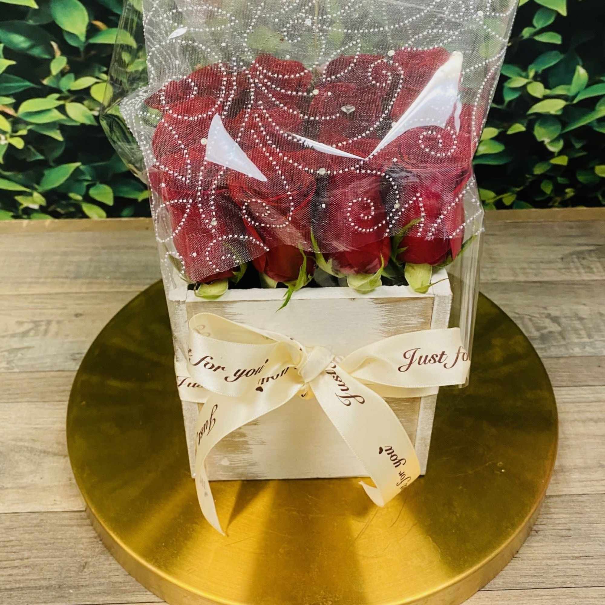 Red roses in a white box wrapped with a sheer decorative cover and ribbon