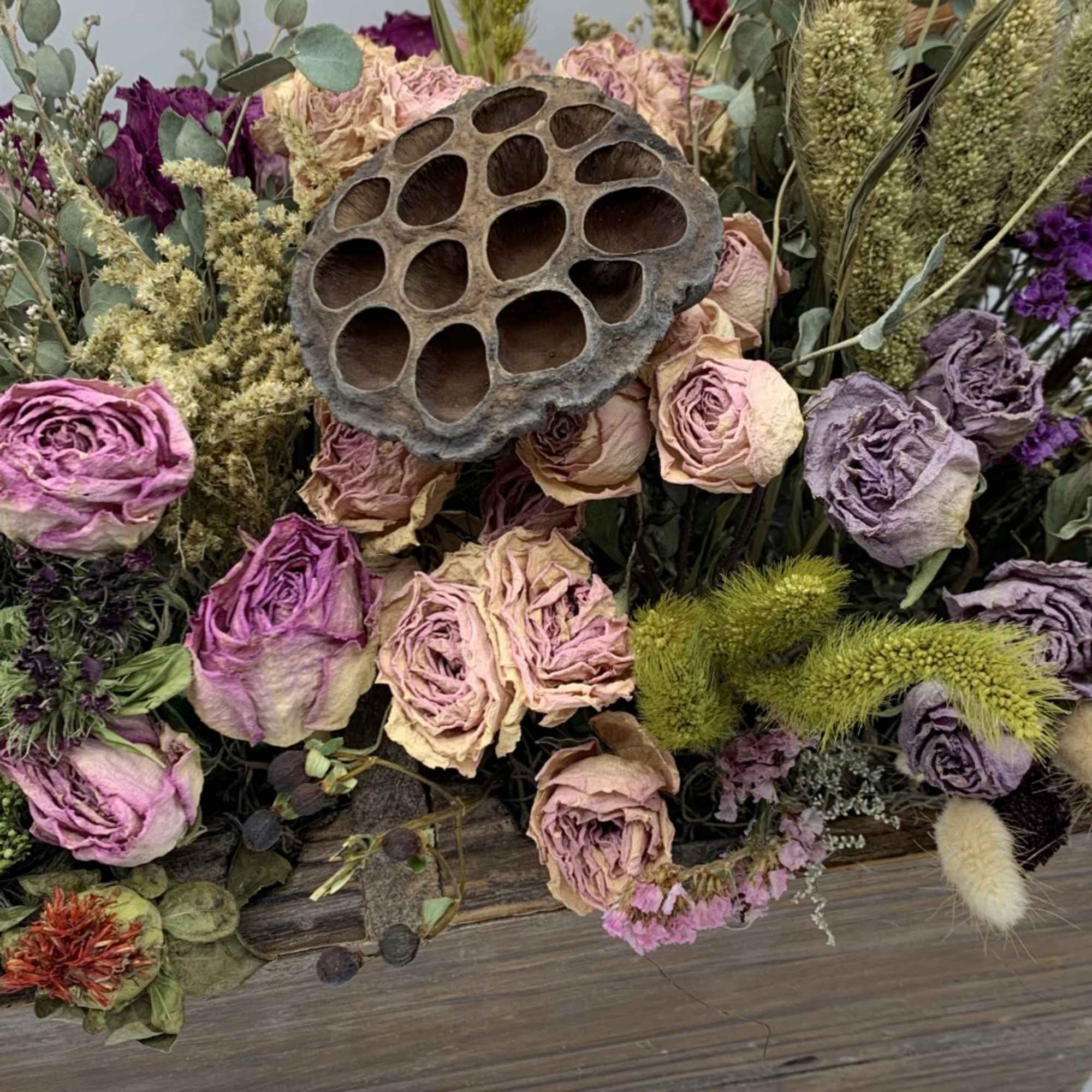Dried roses and grasses arranged around a lotus seed pod in a wooden box