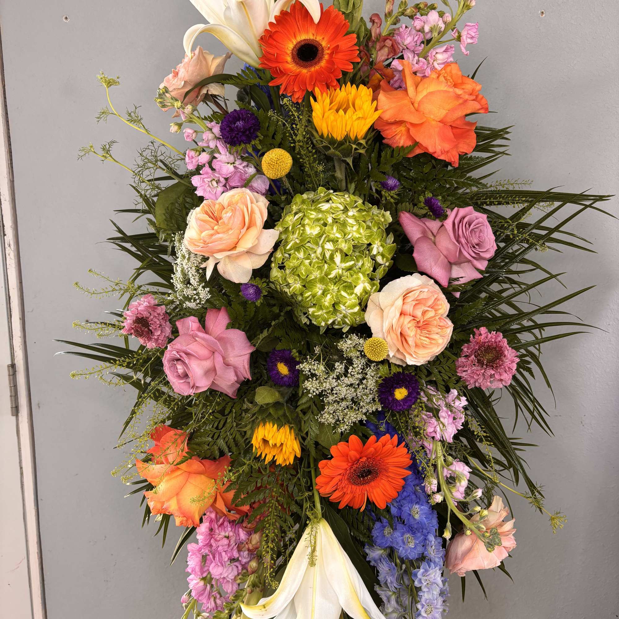 Bright, tall, and unmistakably celebratory, this standing easel spray brings together lilies
