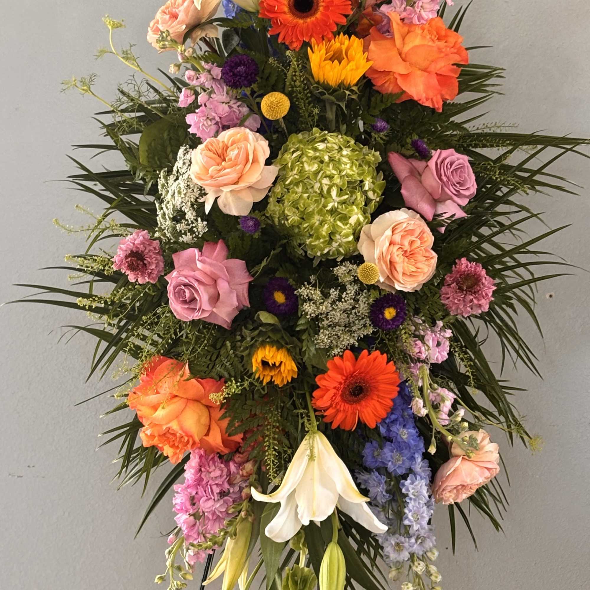 Bright, tall, and unmistakably celebratory, this standing easel spray brings together lilies