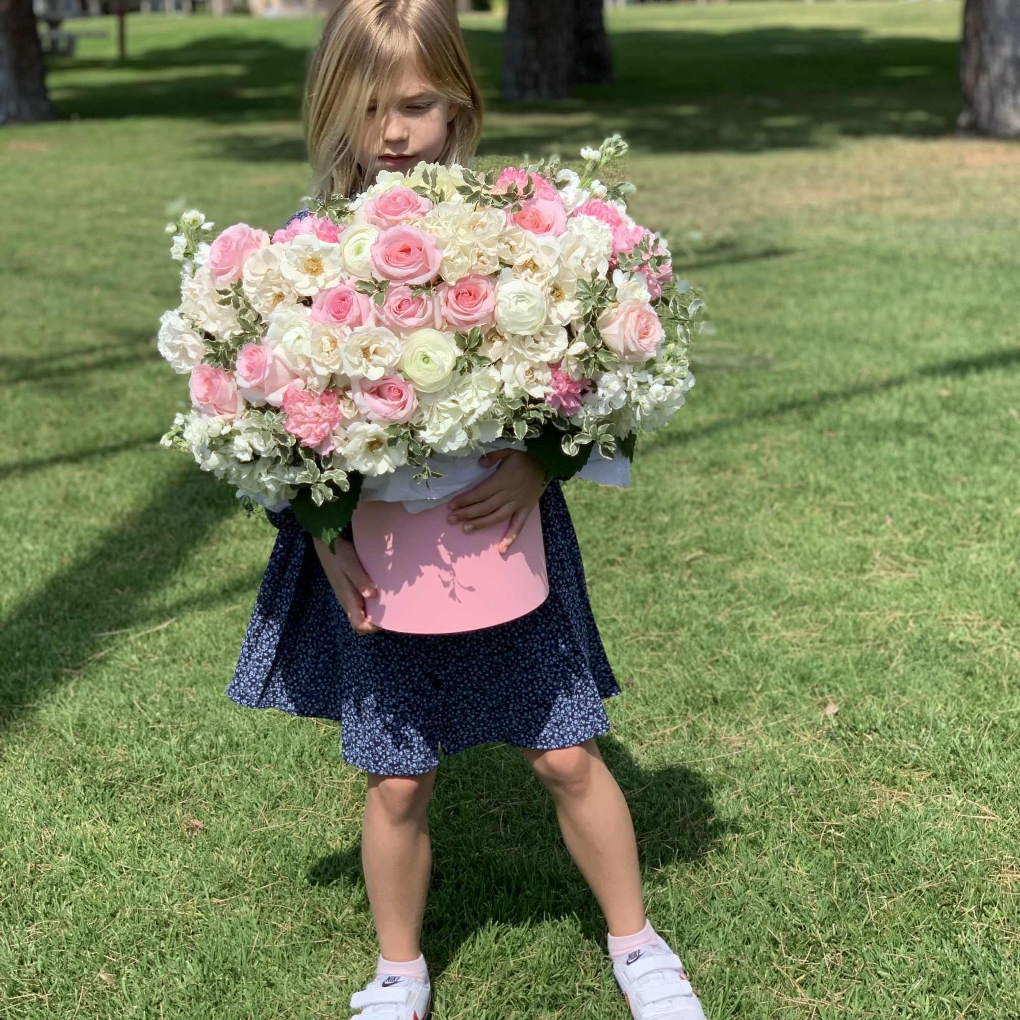 Child holding a large pink and white rose bouquet in a pink box
