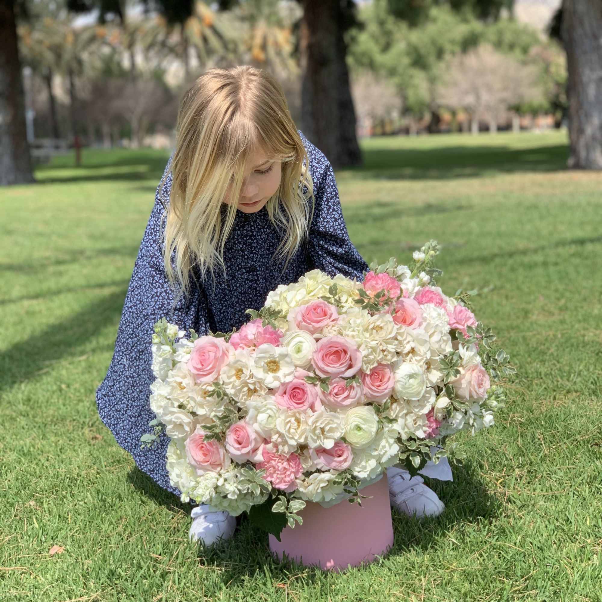 Girl kneeling beside a large pink and white flower arrangement in a round box