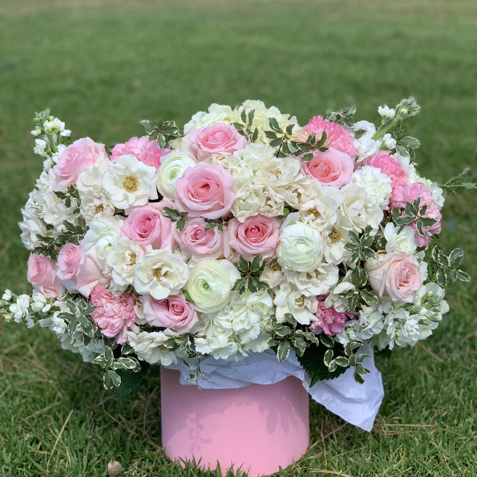 Pink and white floral arrangement in a pink box on grass