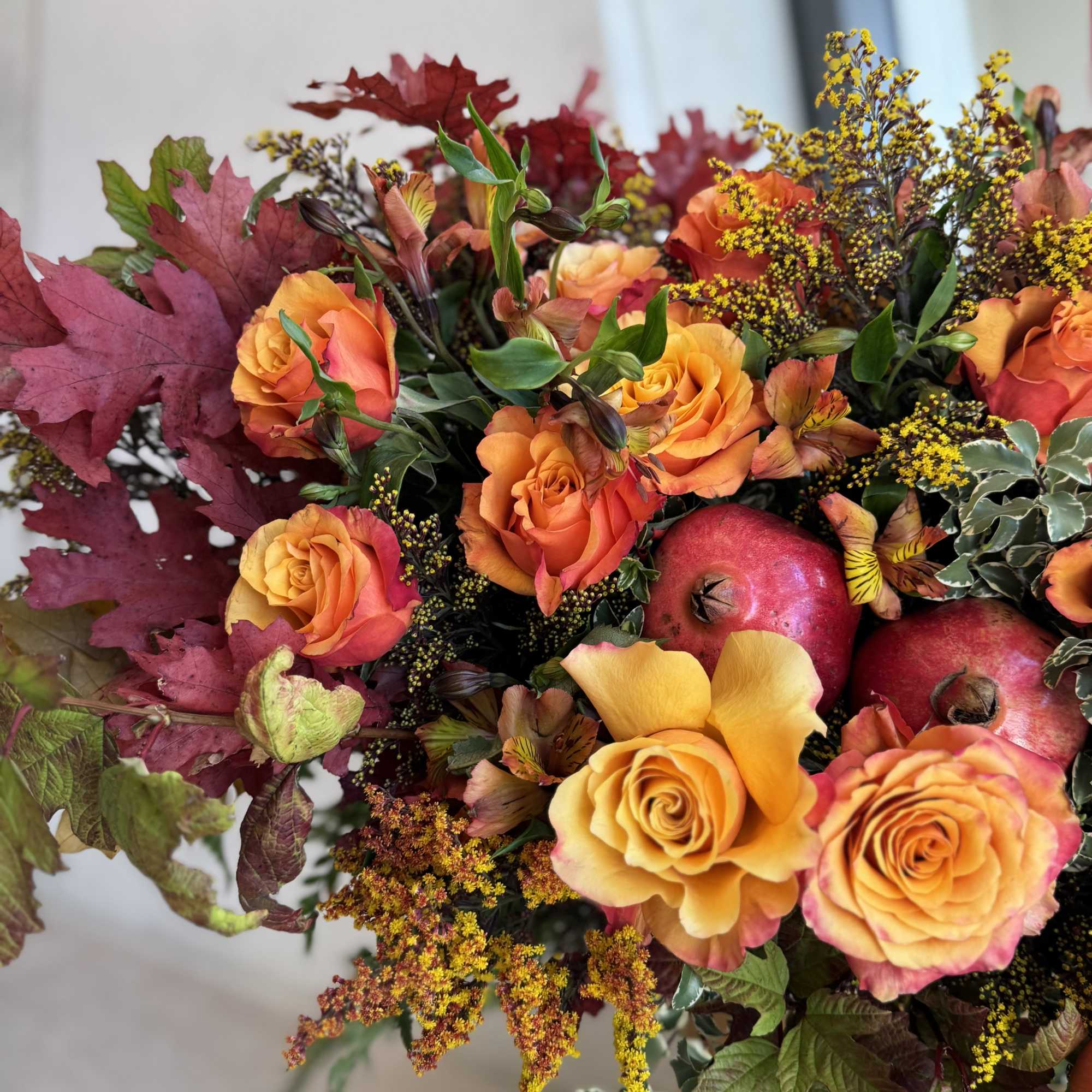 Orange roses with autumn leaves and pomegranates in a bouquet
