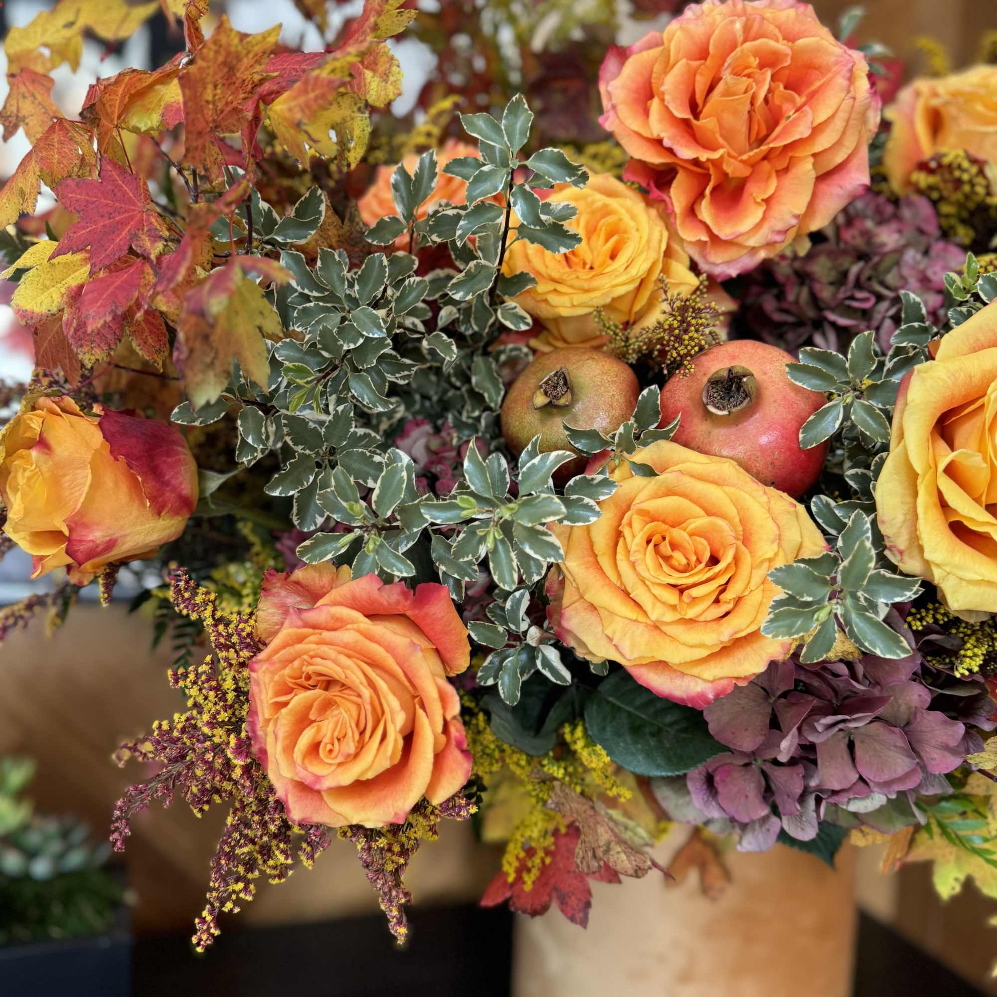 Orange roses arranged with autumn leaves and pomegranates in a vase