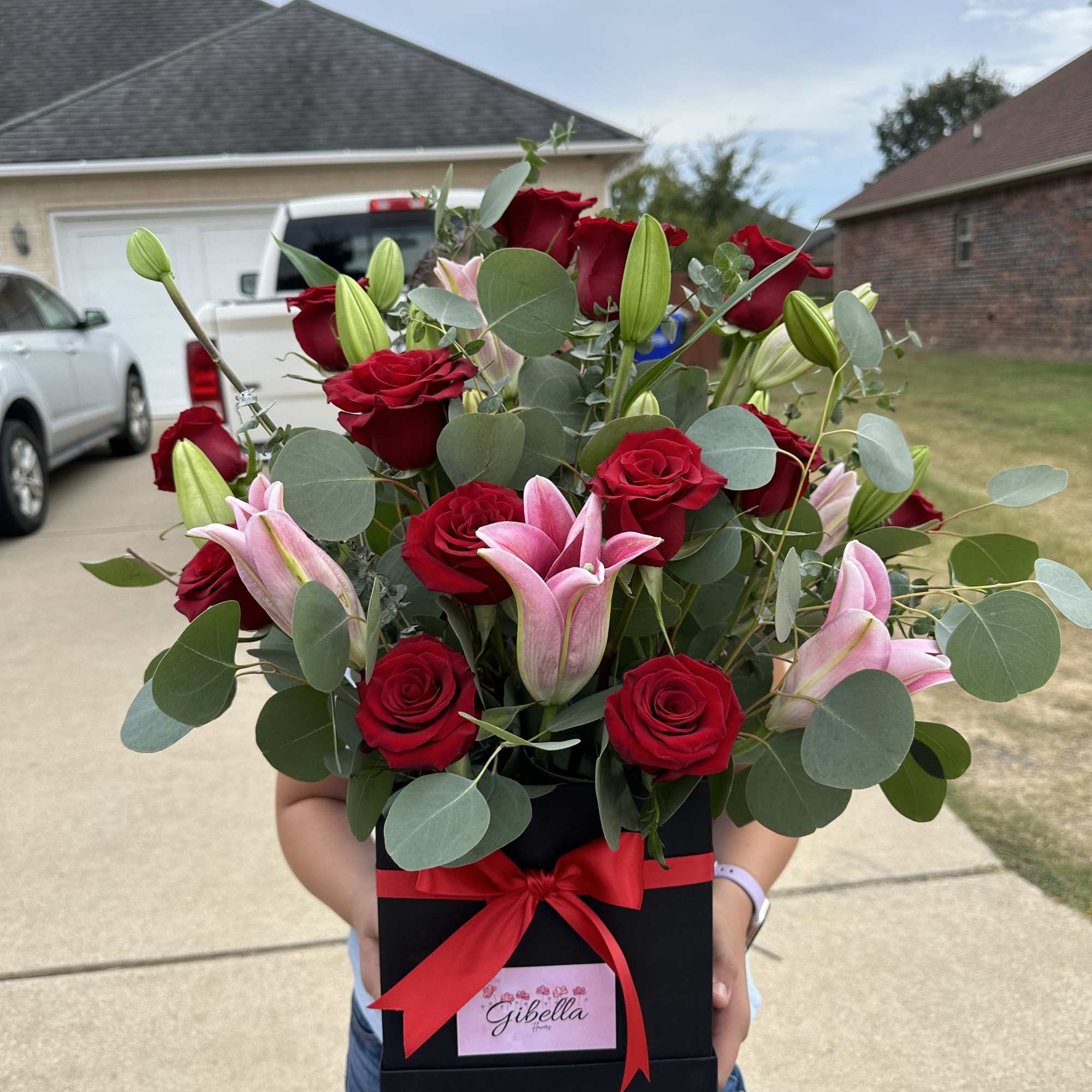Bouquet of red roses and pink lilies in a black gift box with a red ribbon