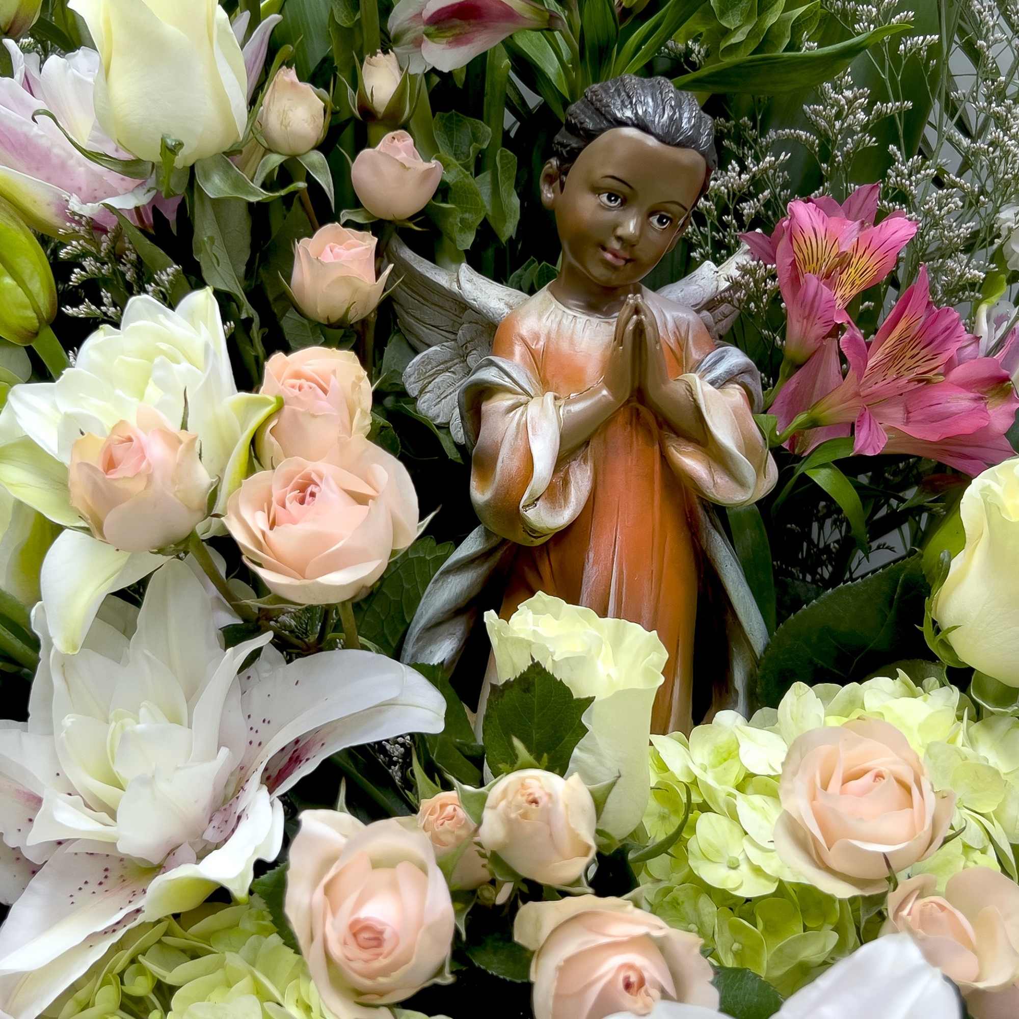 Floral arrangement with roses, lilies, and a praying angel figurine