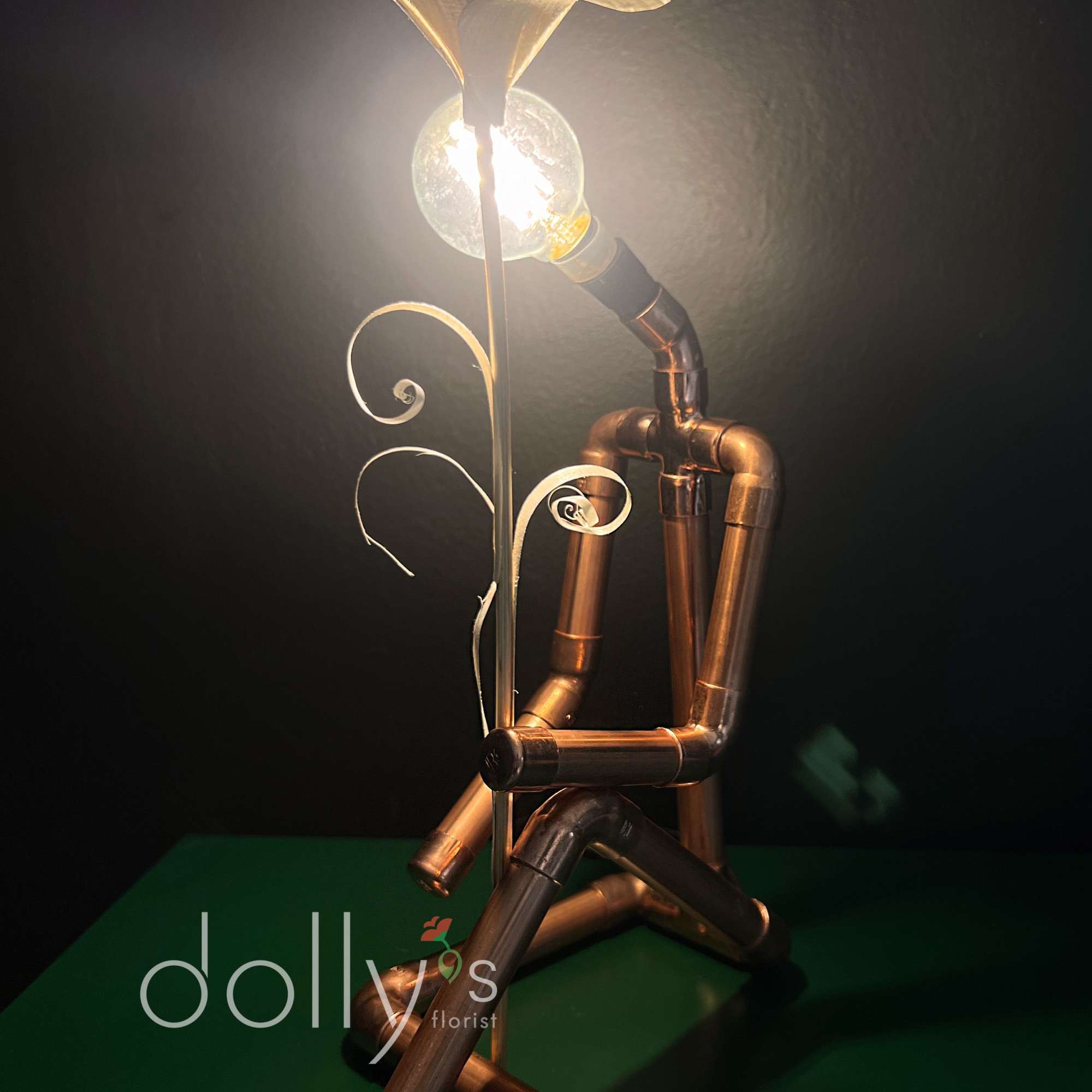 A decorative lamp made from copper pipes with a glowing bulb and leaf-shaped top.