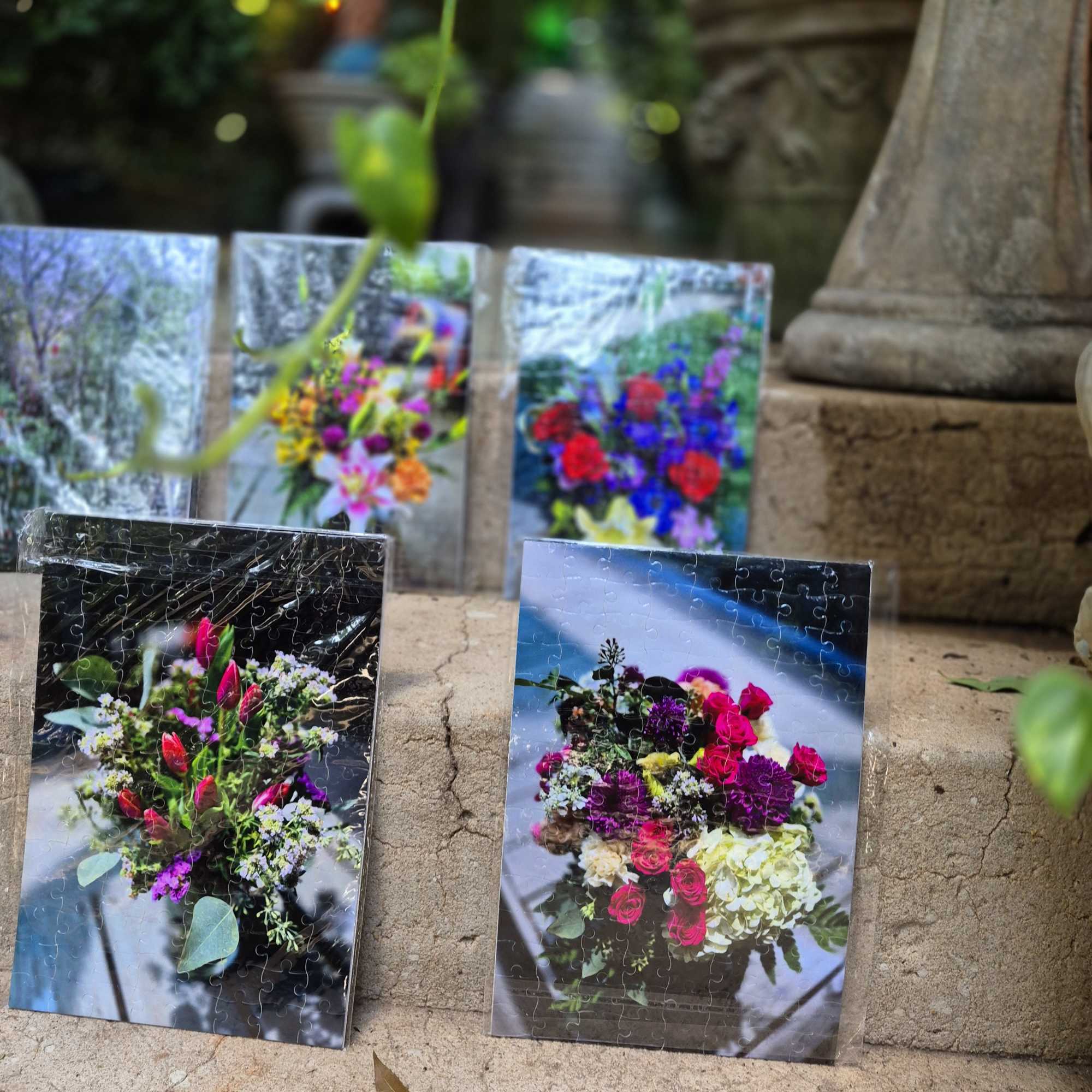 Four floral puzzle prints leaning on a stone step outdoors.