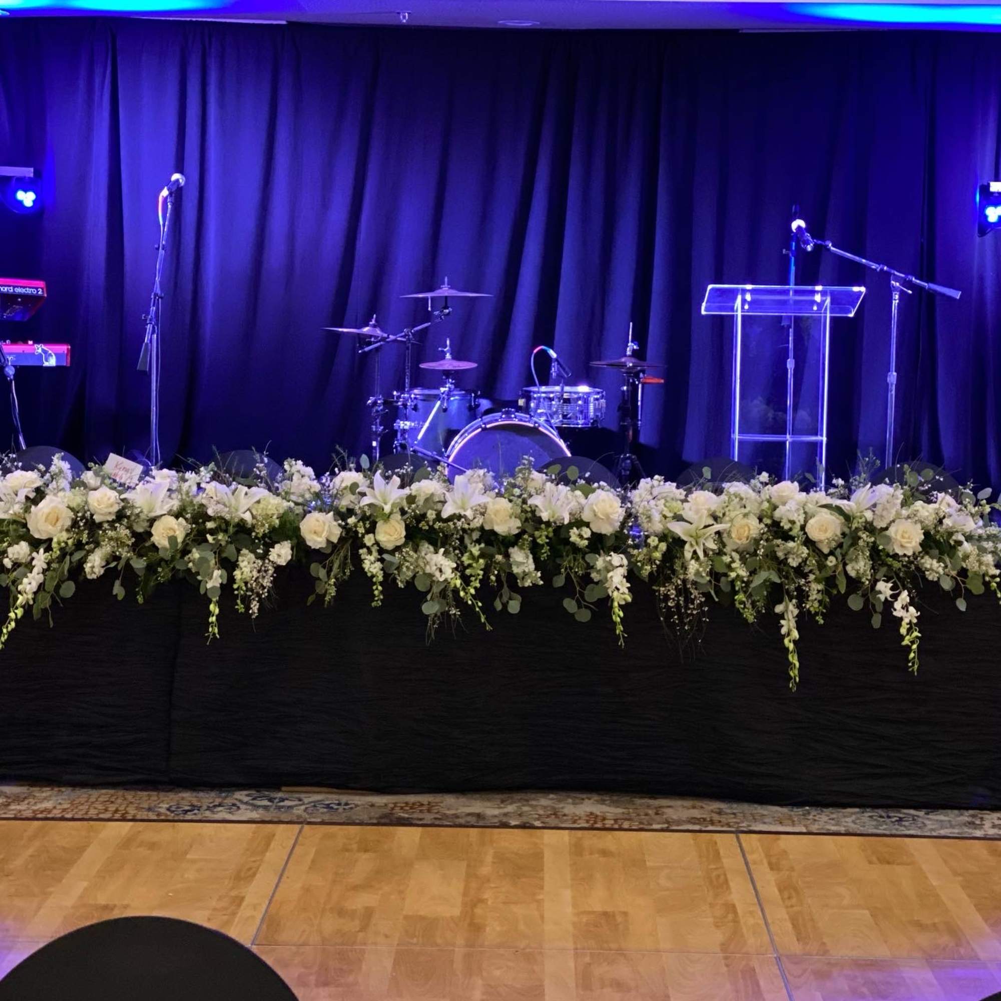 Long white floral arrangement across a stage in front of microphones and a podium
