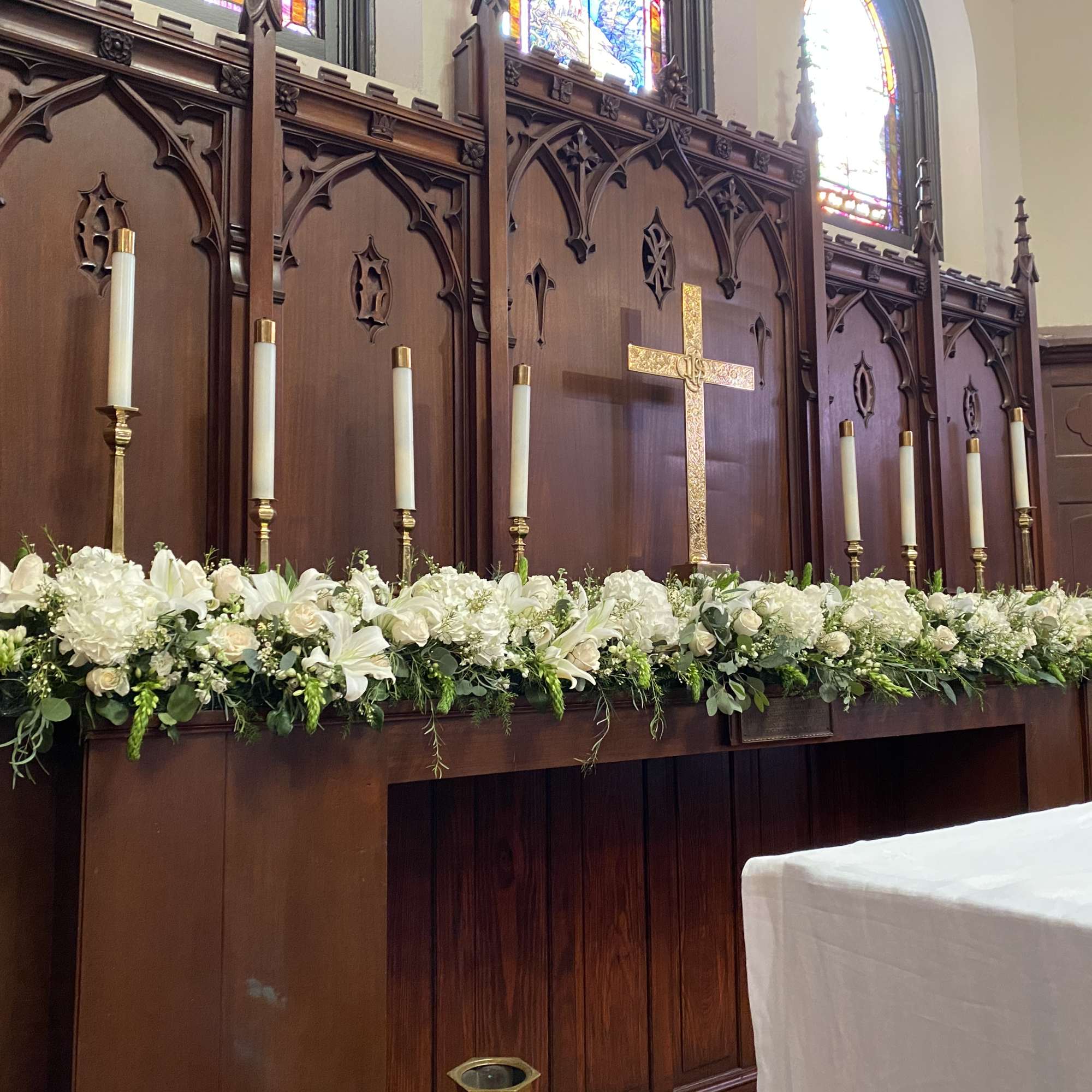 White floral altar arrangement with candles and a gold cross in a church