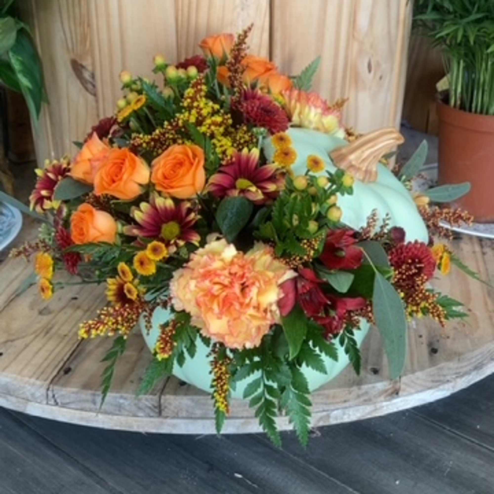 Autumn floral arrangement with orange roses and burgundy blooms around a pale blue pumpkin