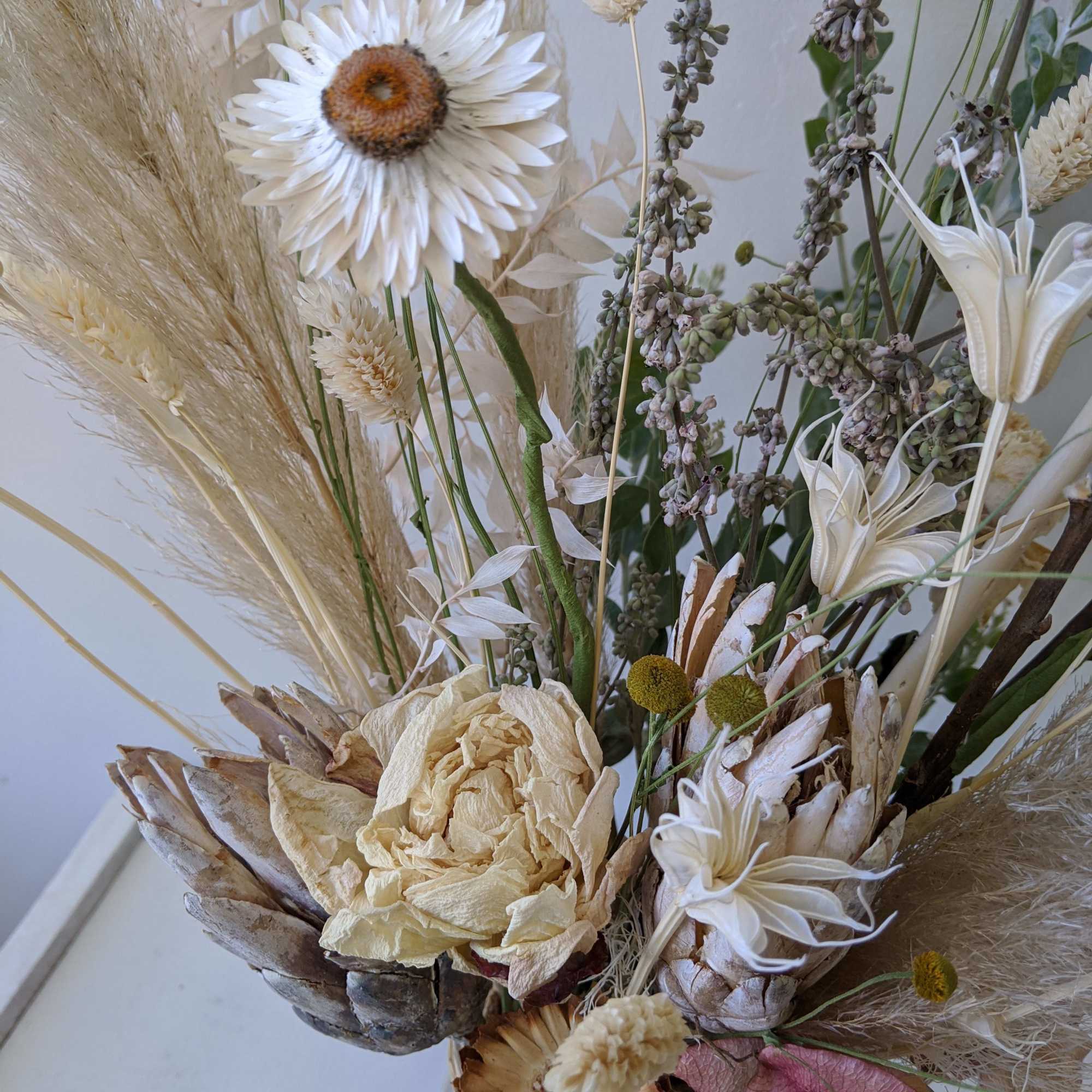 Dried floral arrangement with cream blooms and tall grasses in a vase