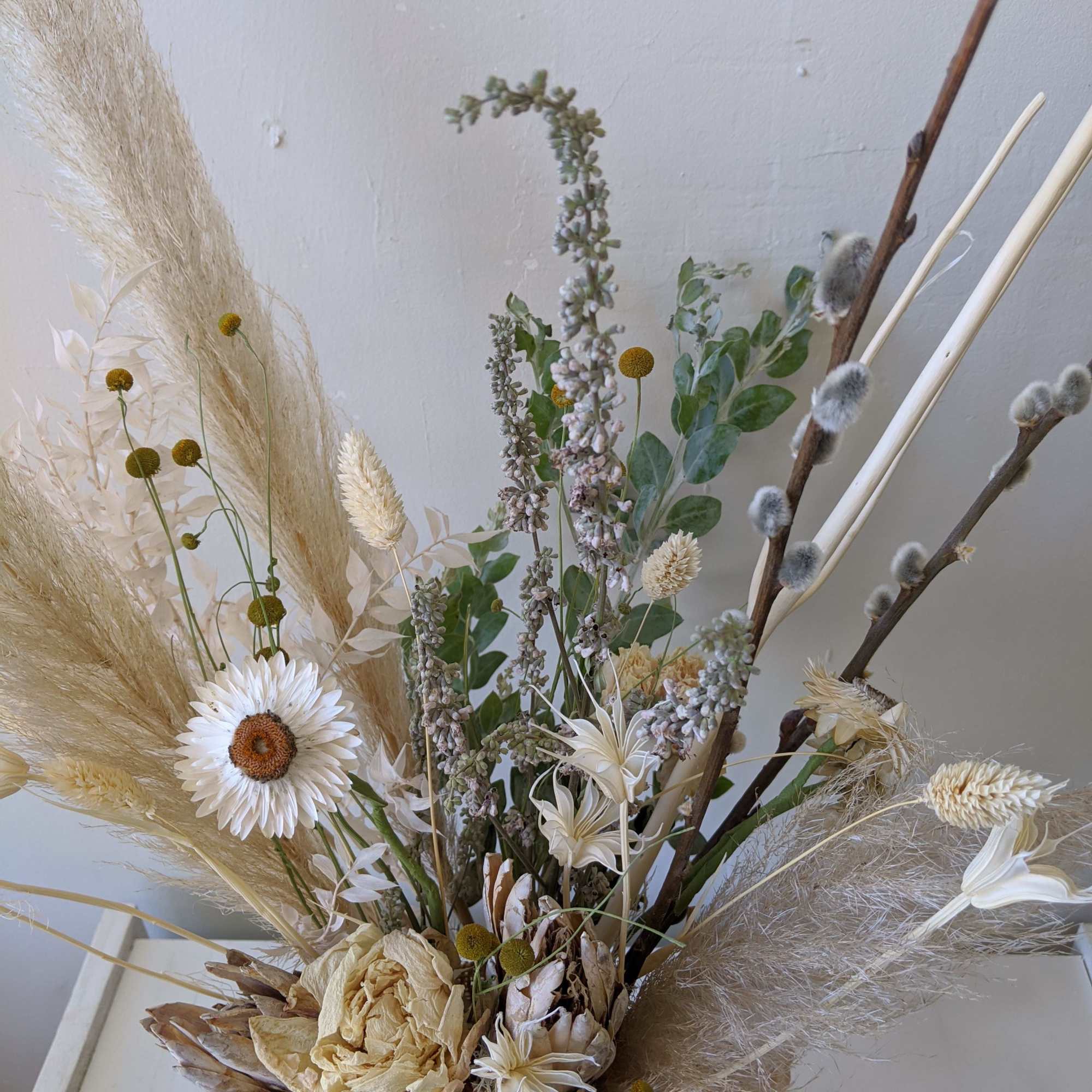 Dried floral arrangement with white blooms and beige grasses in a vase
