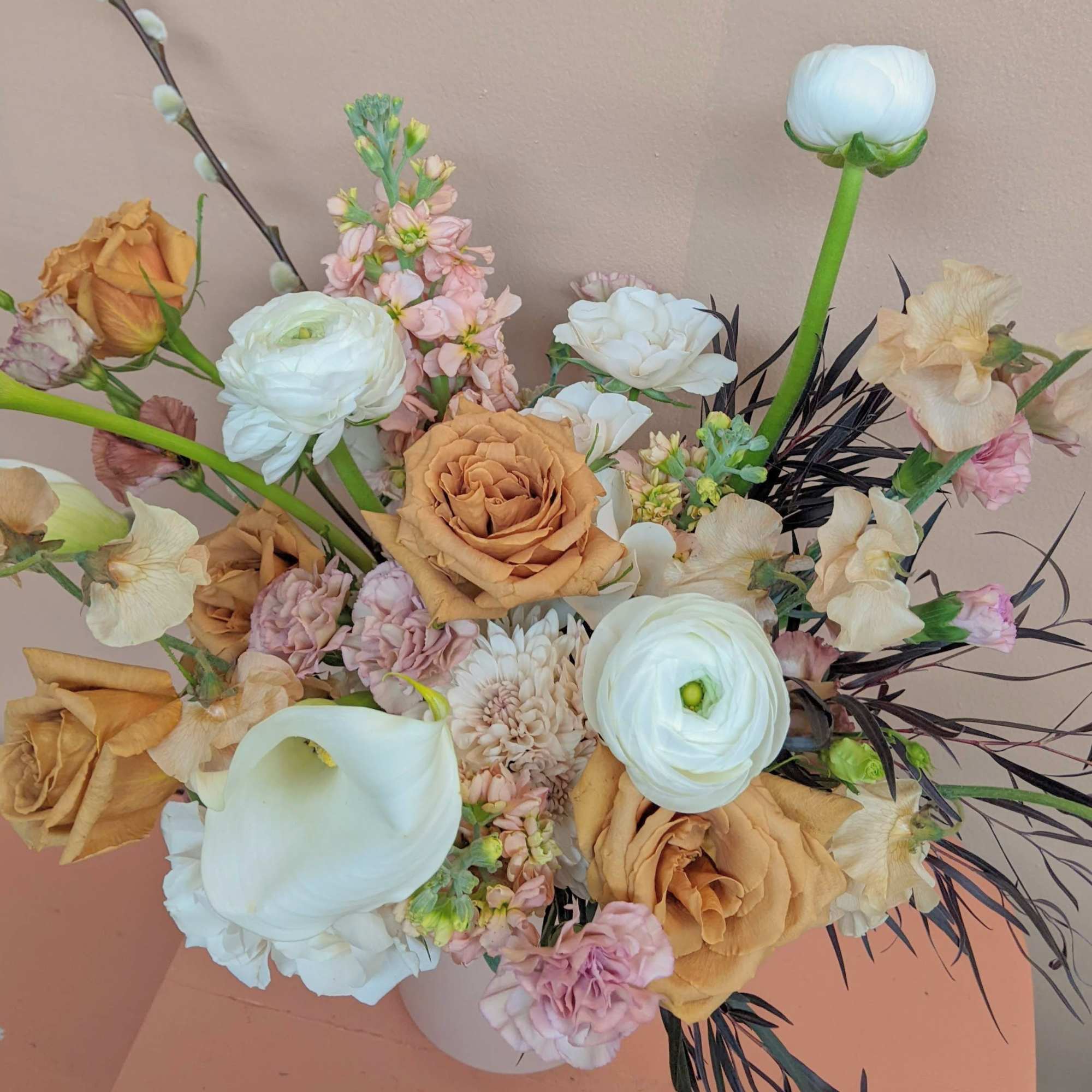 Bouquet of peach roses, white ranunculus, and pale pink flowers in a vase