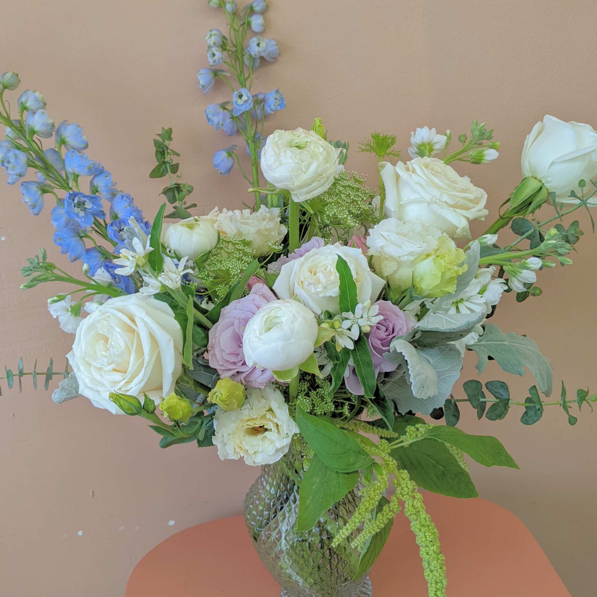 Mixed bouquet of white roses, pale blooms, and blue flowers in a glass vase