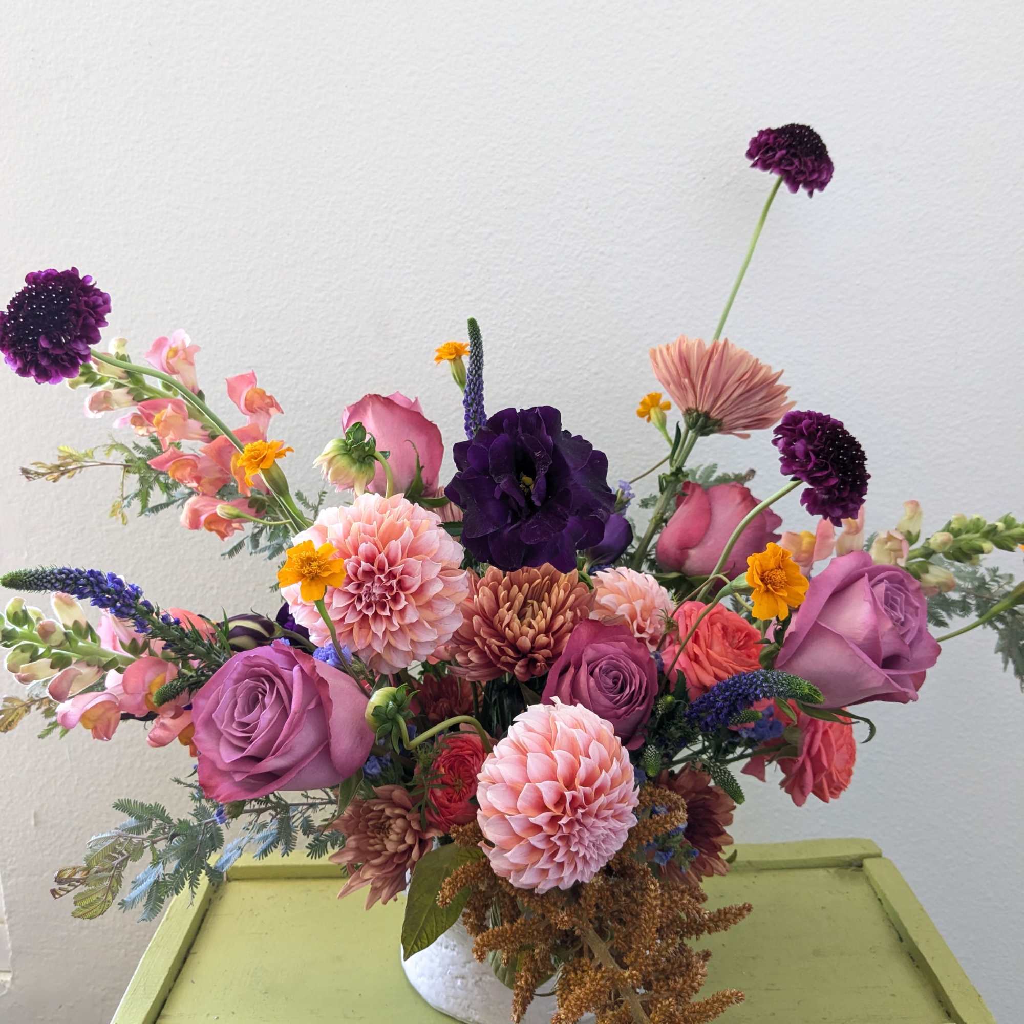 Mixed bouquet of pink, purple, and peach flowers in a white vase