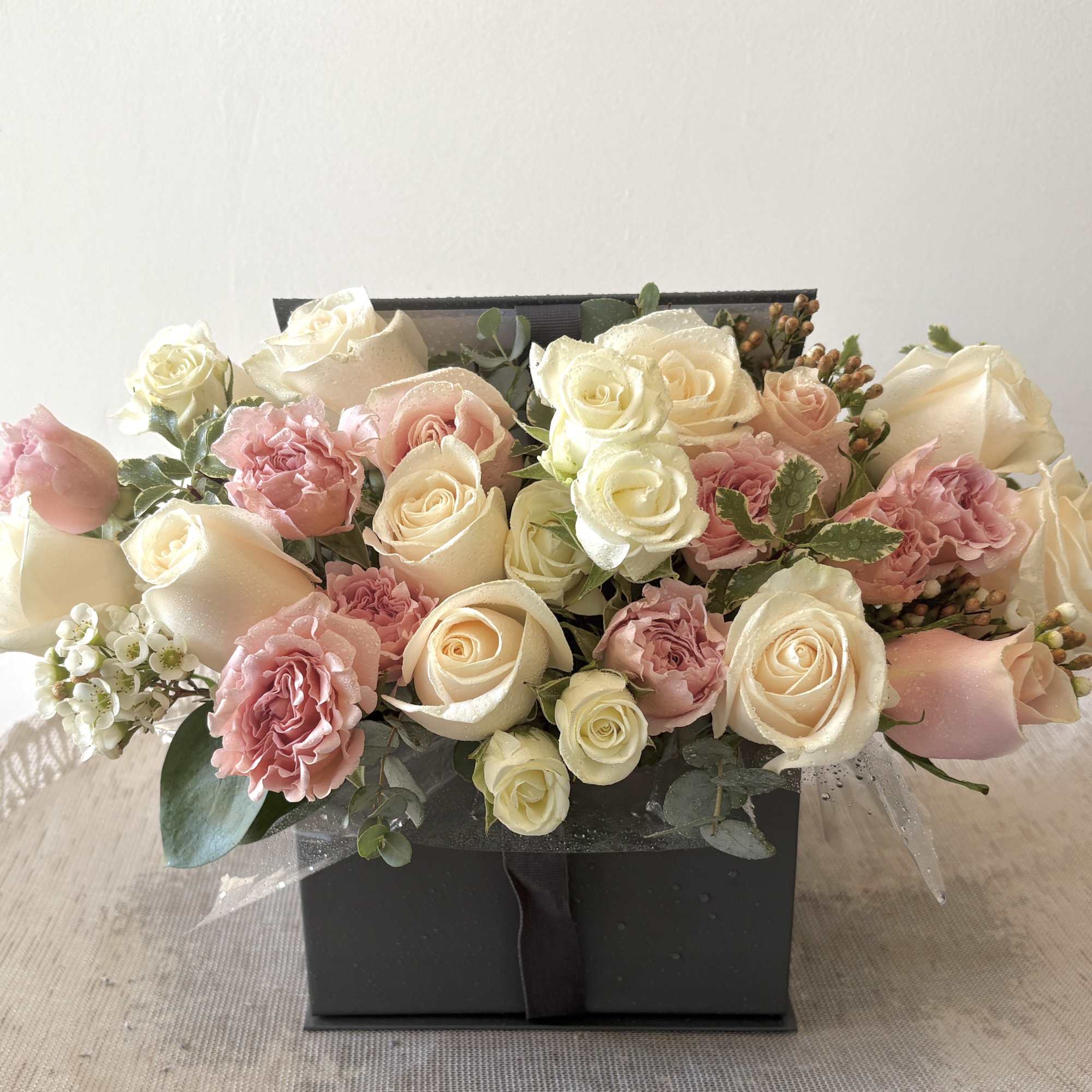 Pink and cream roses arranged in a black gift box