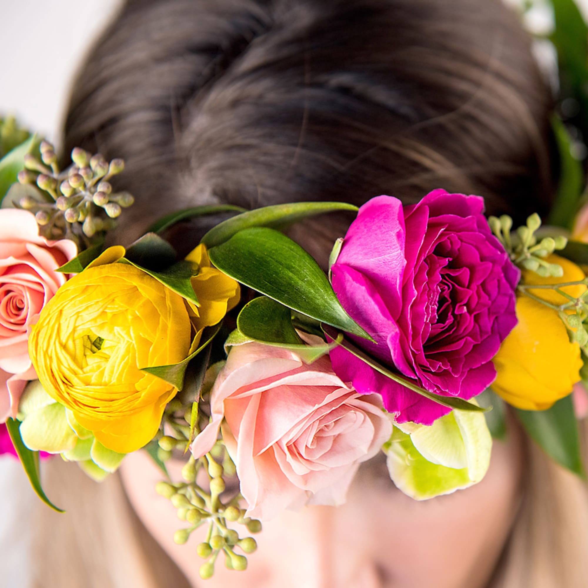 Bright flower crown with pink roses and yellow ranunculus worn on top of a woman's head