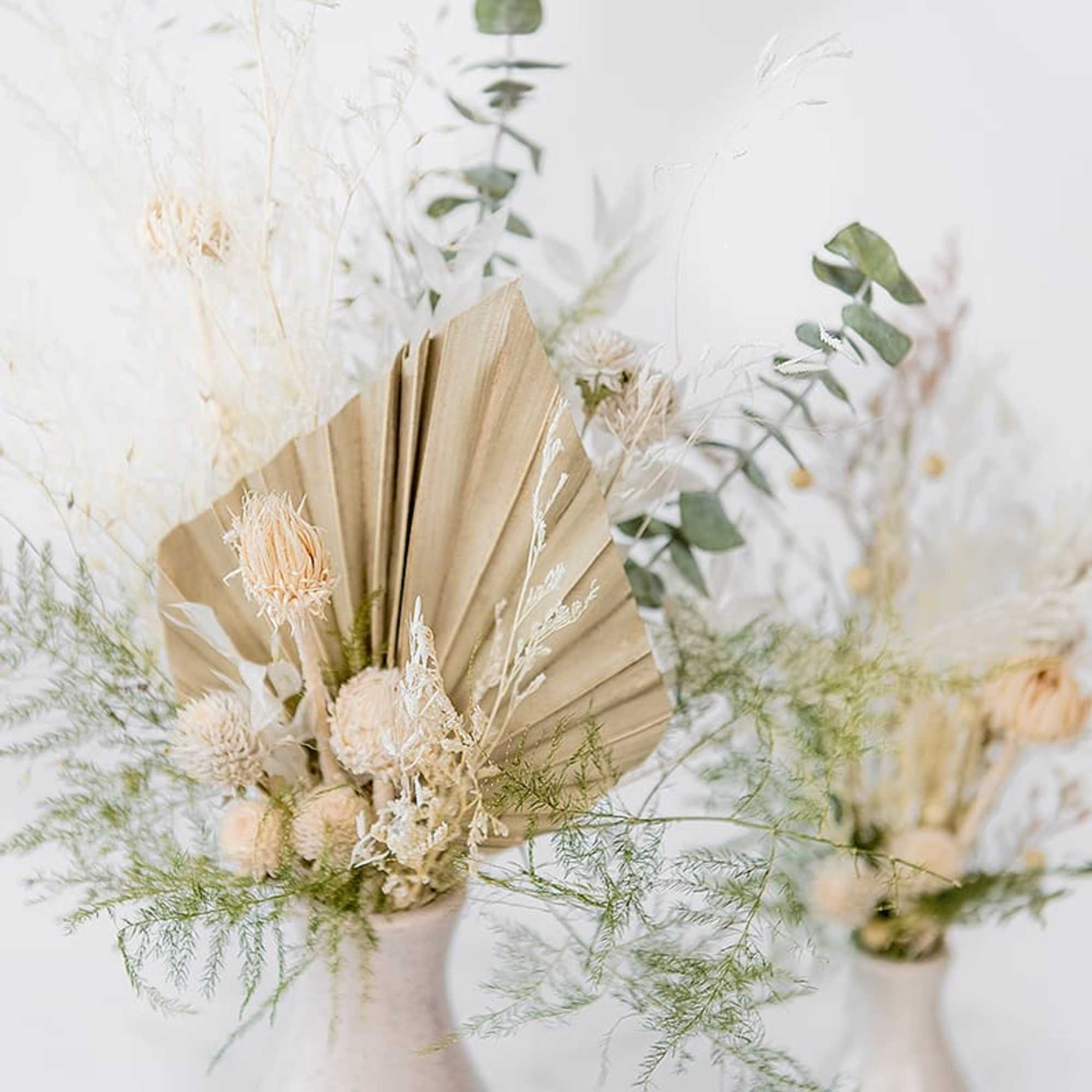 Dried floral arrangement in a white vase with beige fan-shaped accents