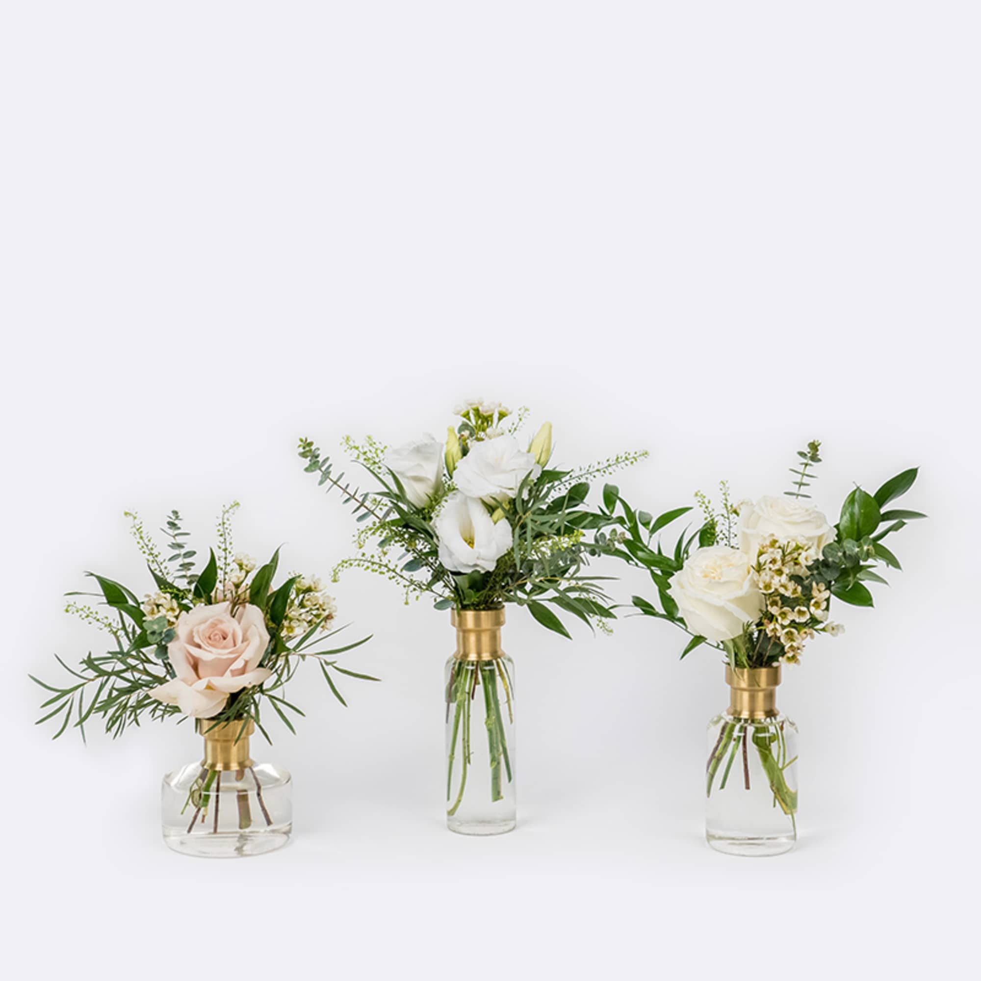 Three small floral arrangements in glass vases with white and blush roses