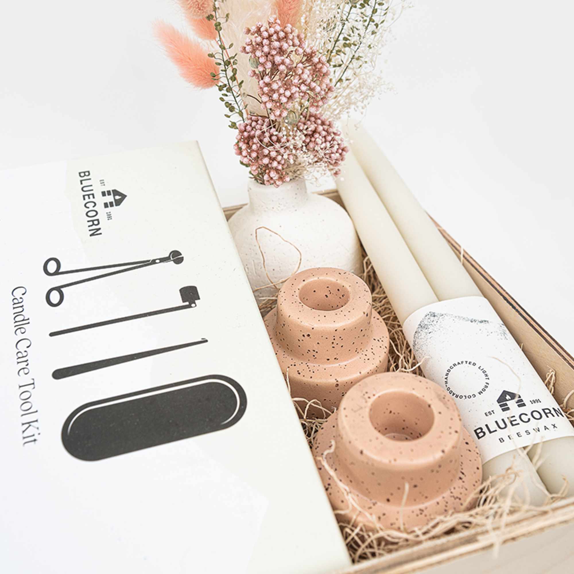 Gift box with candles, a candle care tool kit, and a small dried floral arrangement