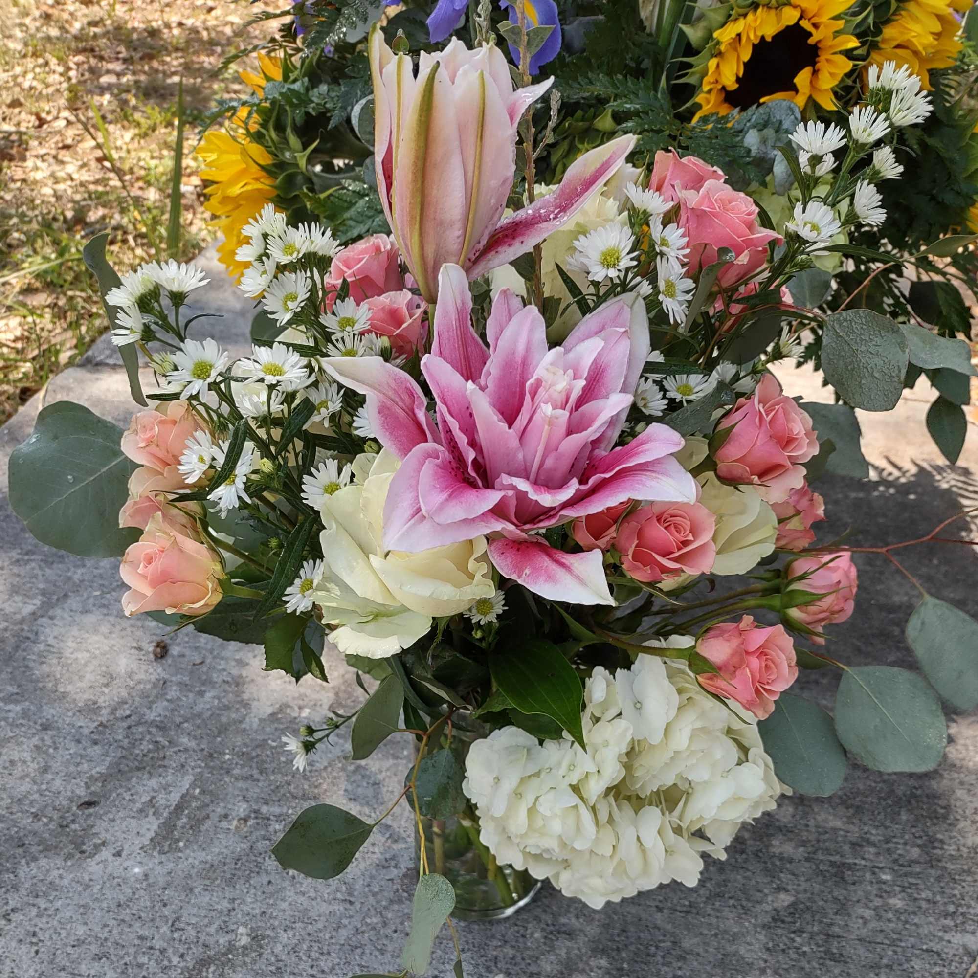 Pink lilies and roses arranged with white daisies in a glass vase.
