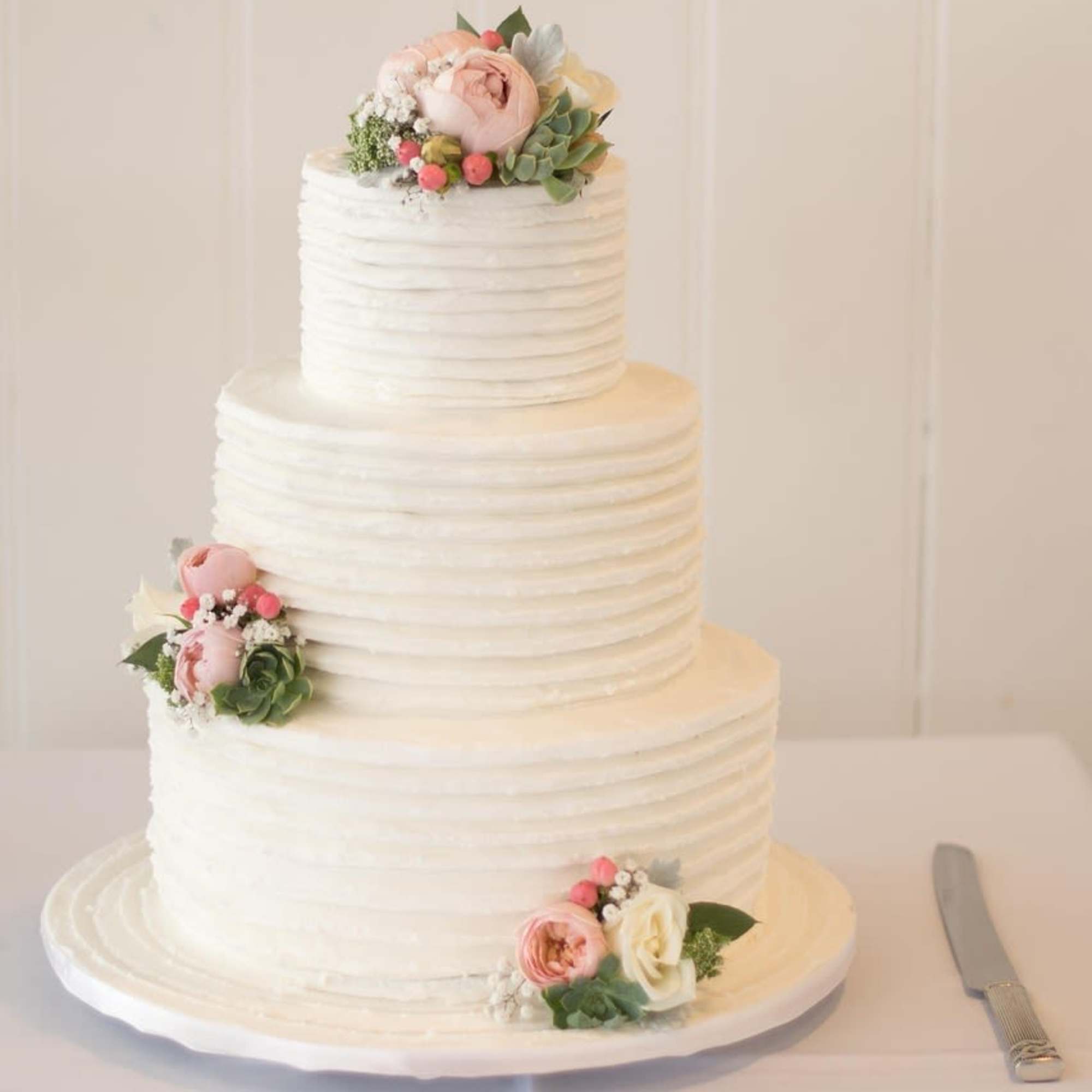 Three-tier white cake decorated with blush and ivory flowers and succulents.