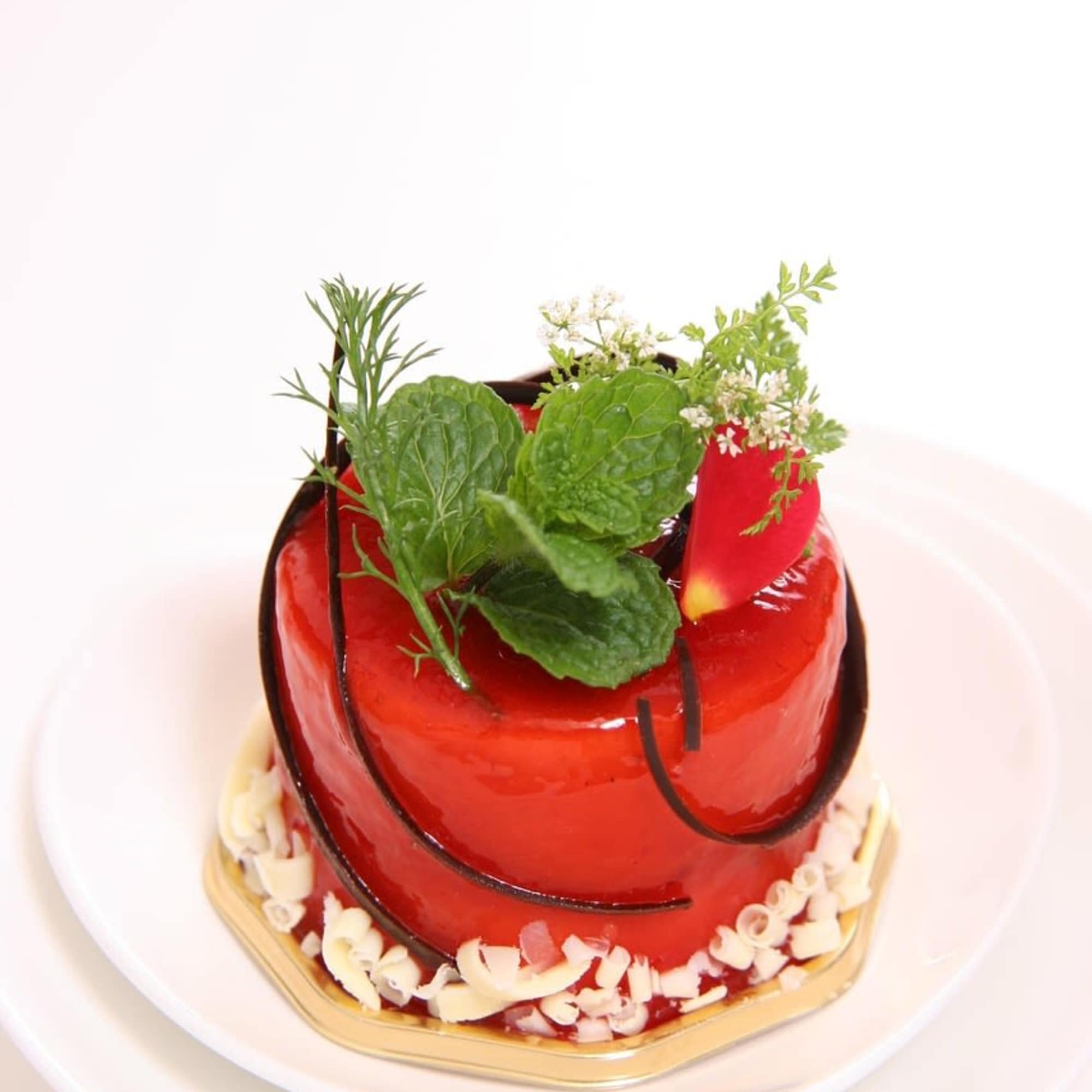 Small red glazed cake topped with fresh herb sprigs on a white plate