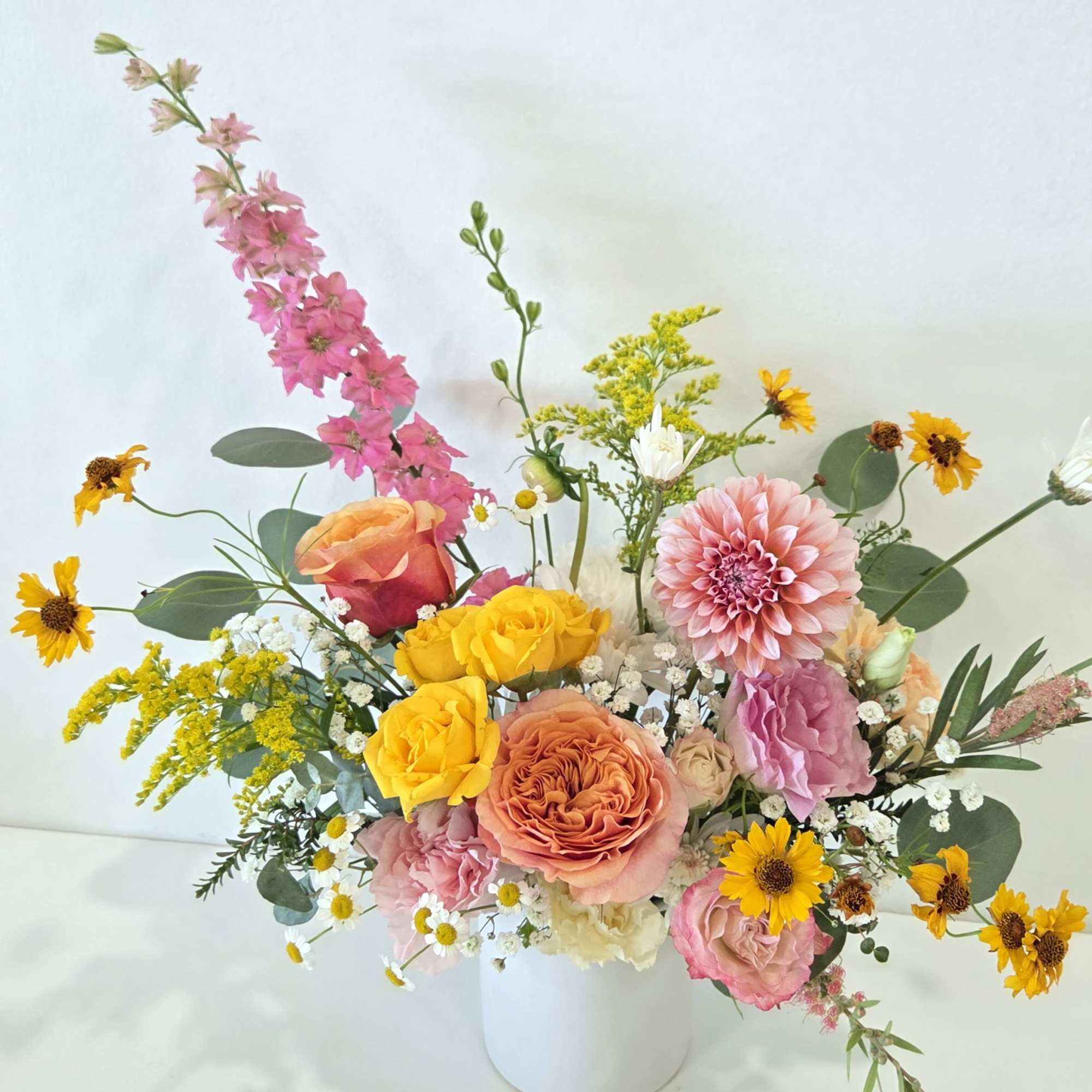 Mixed bouquet of pink, yellow, and peach flowers in a white vase